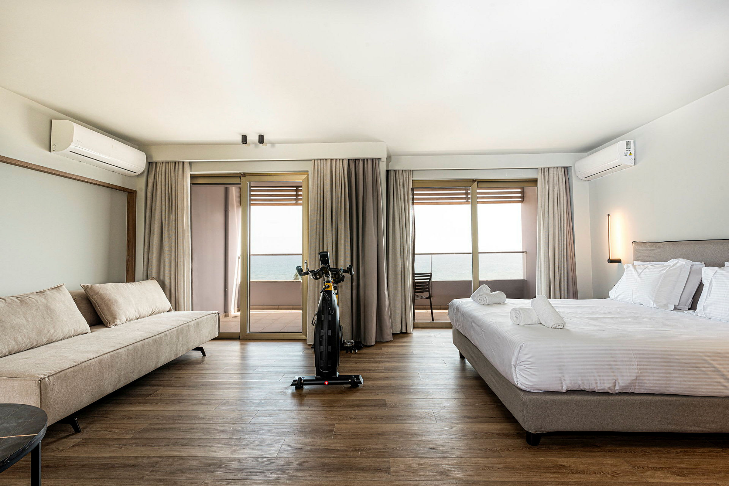 Et hotelværelse med en seng og en sofa, udsigt til en balkon og havet. (AI-genereret tekst)
