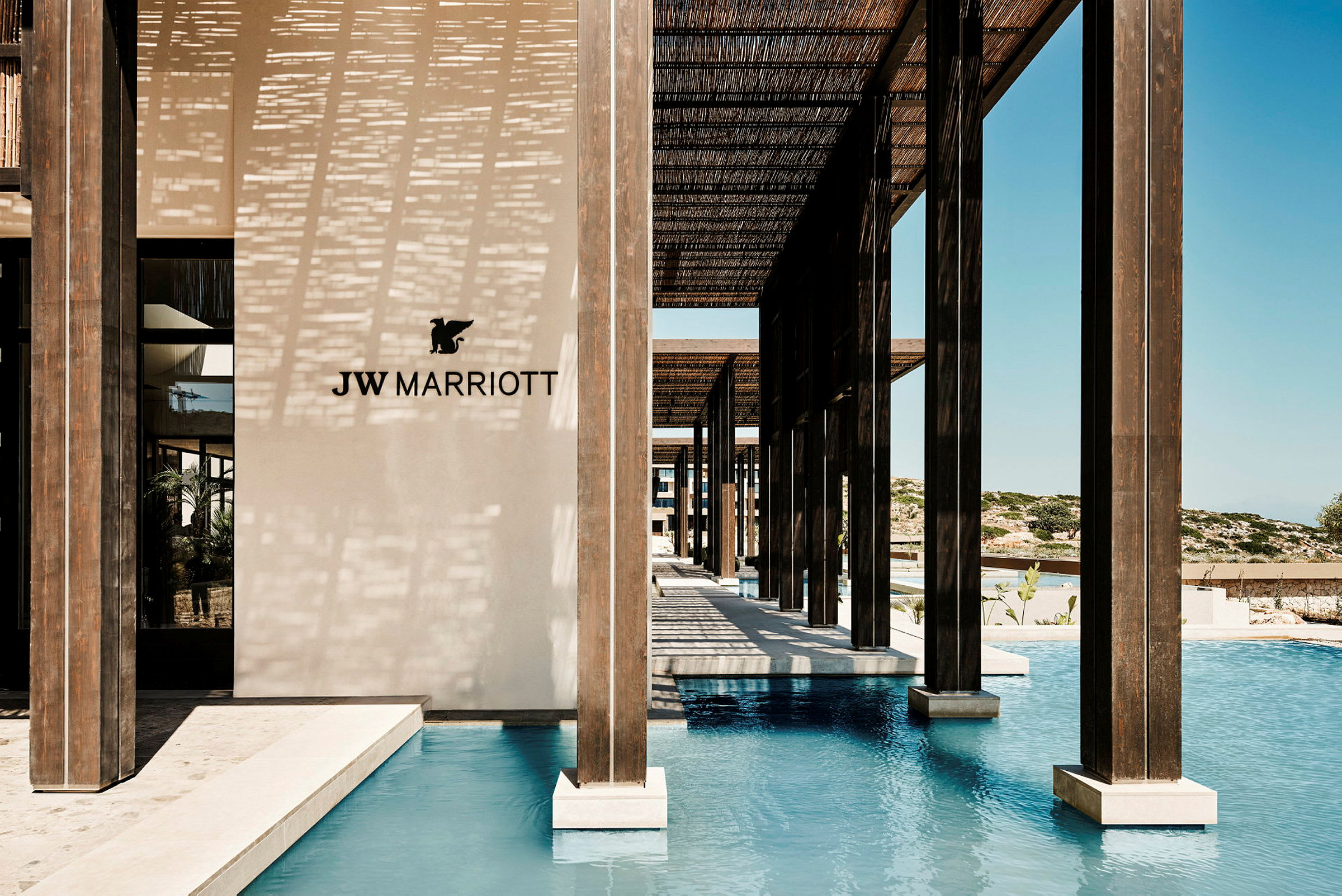JW Marriott-logo på en lys væg ved en pool med træstolper. (AI-genereret tekst)