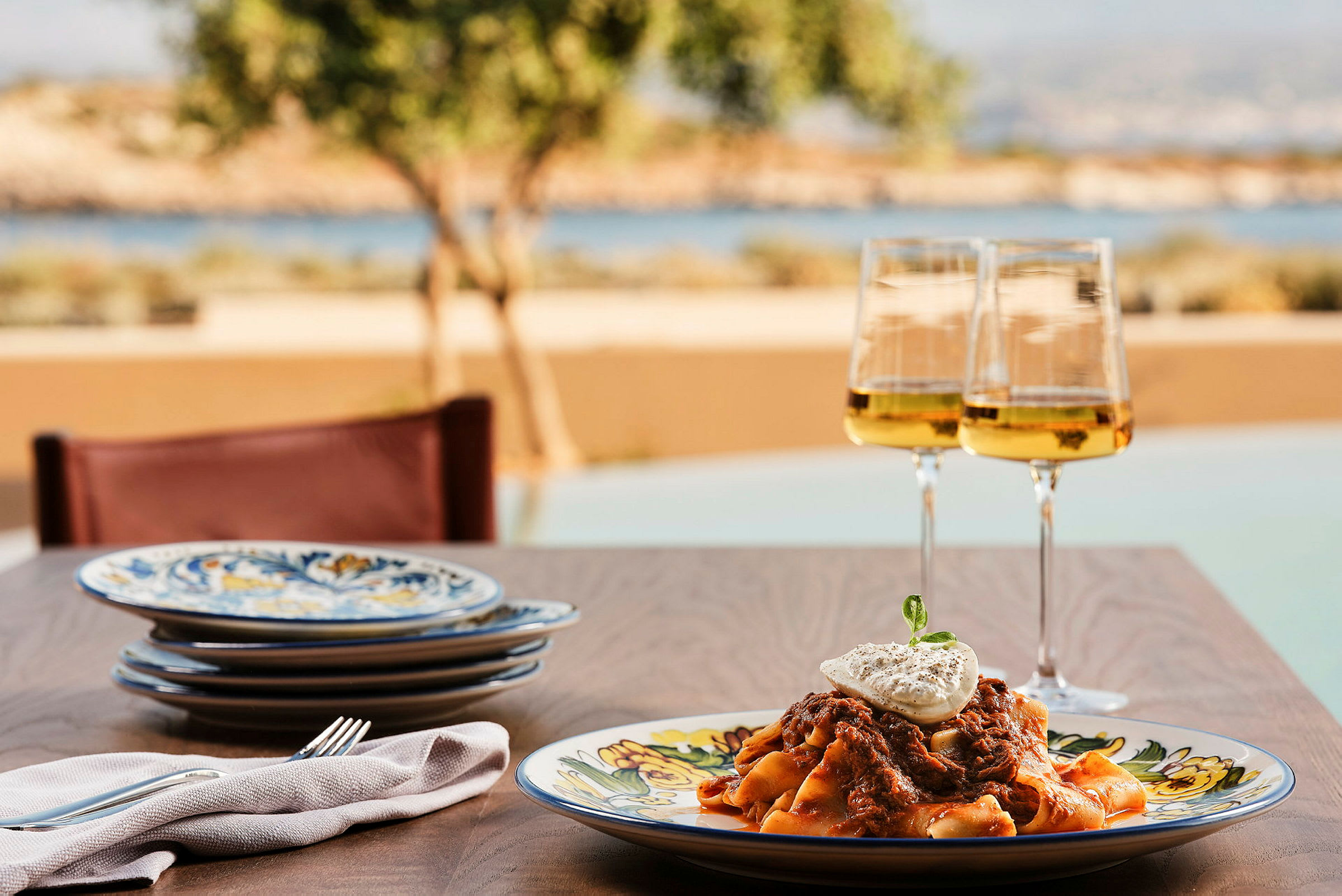 En tallerken med pasta og et glas hvidvin på et bord med udsigt til naturen. (AI-genereret tekst)