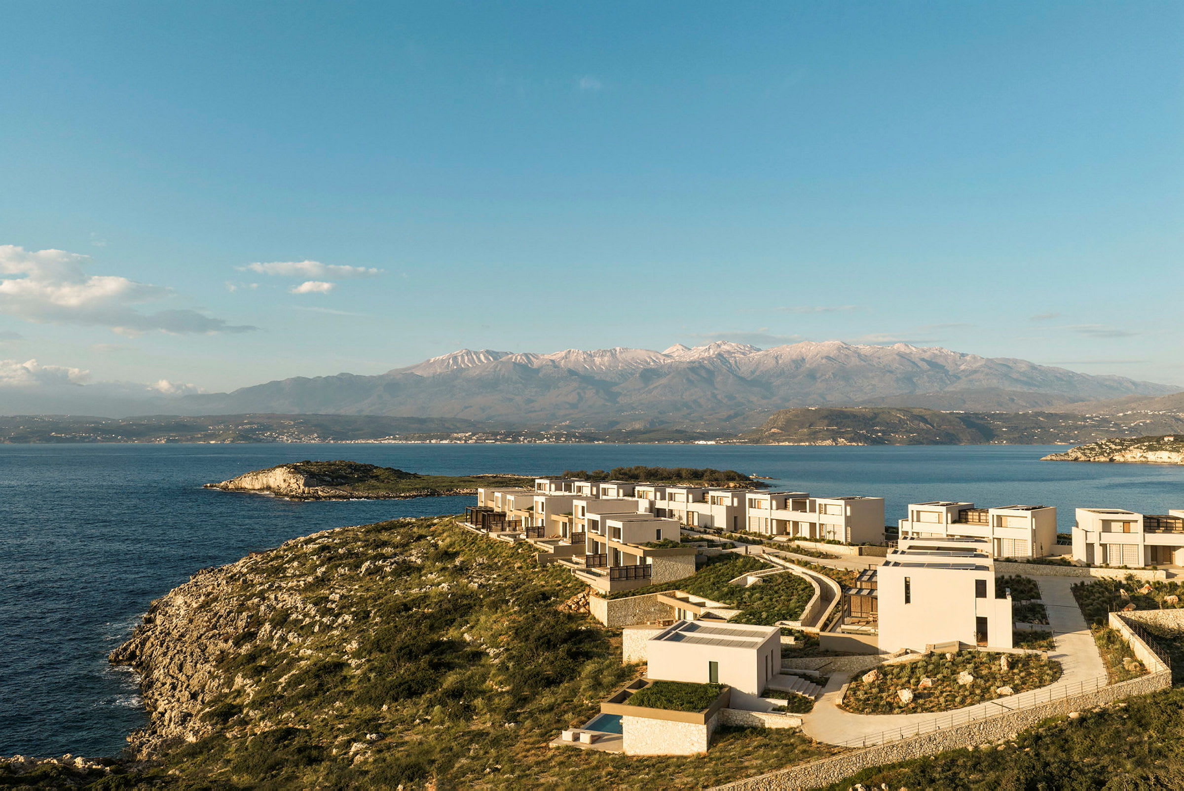 En kystlinje med moderne arkitektur nær havet og bjerge i baggrunden. (AI-genereret tekst)