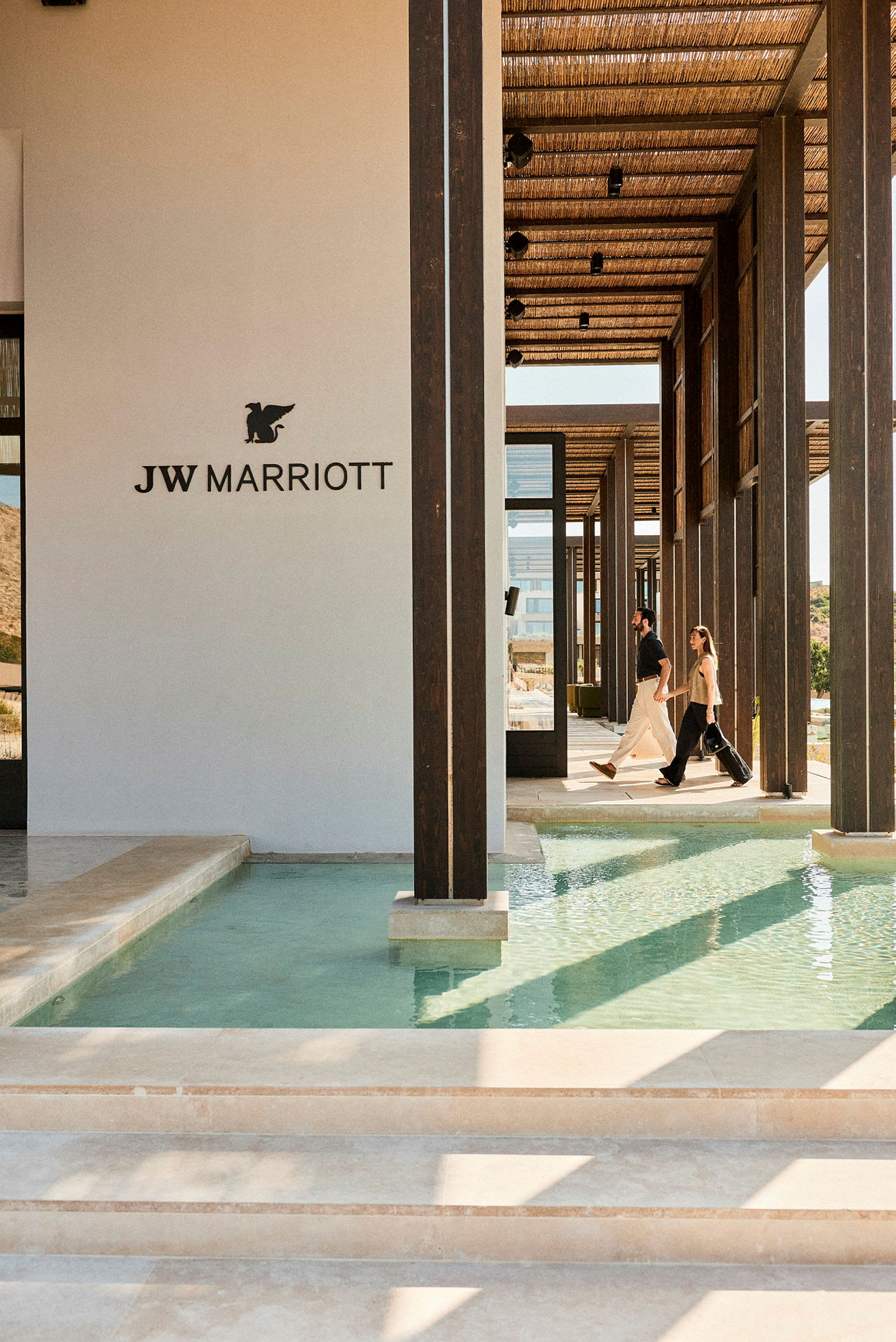 Billede af en moderne bygning med JW Marriott-logoen, hvor folk går langs en gang med vand på begge sider. (AI-genereret tekst)