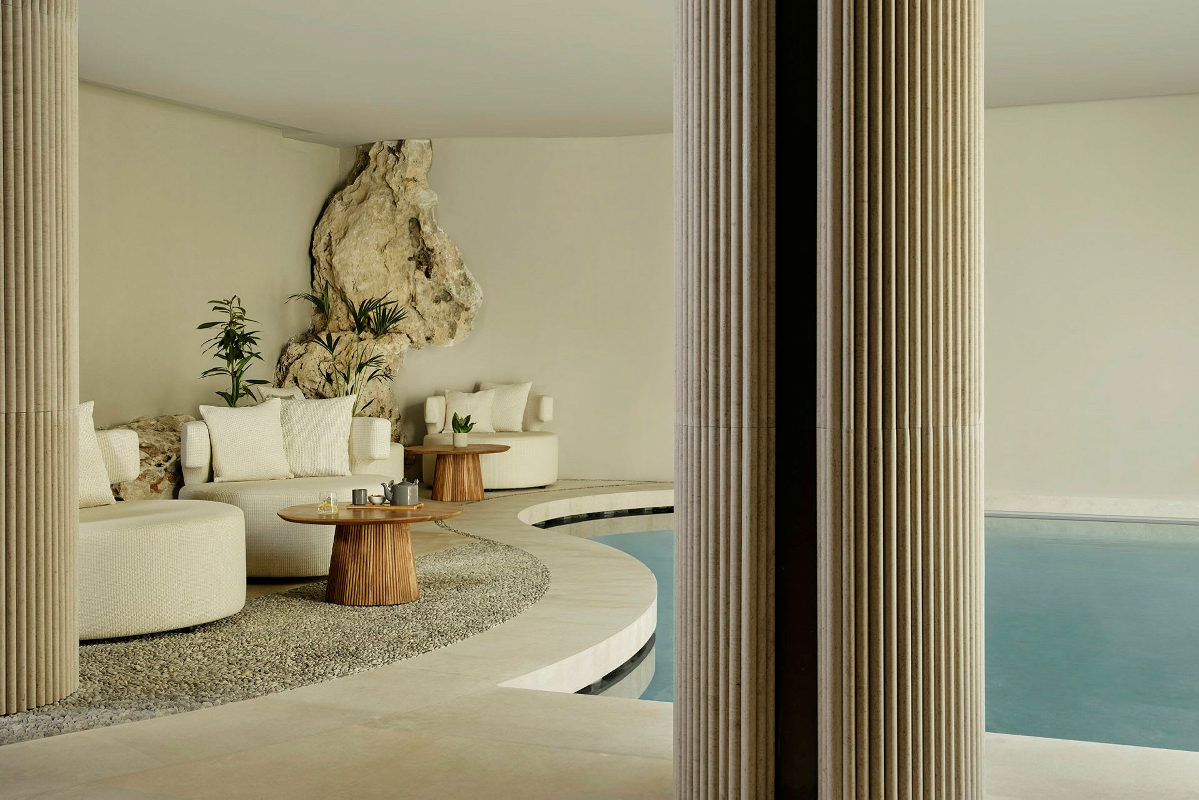 Et elegant indendørsområde med siddepladser, træborde og en pool, omgivet af sten- og plantetilbehør. (AI-genereret tekst)
