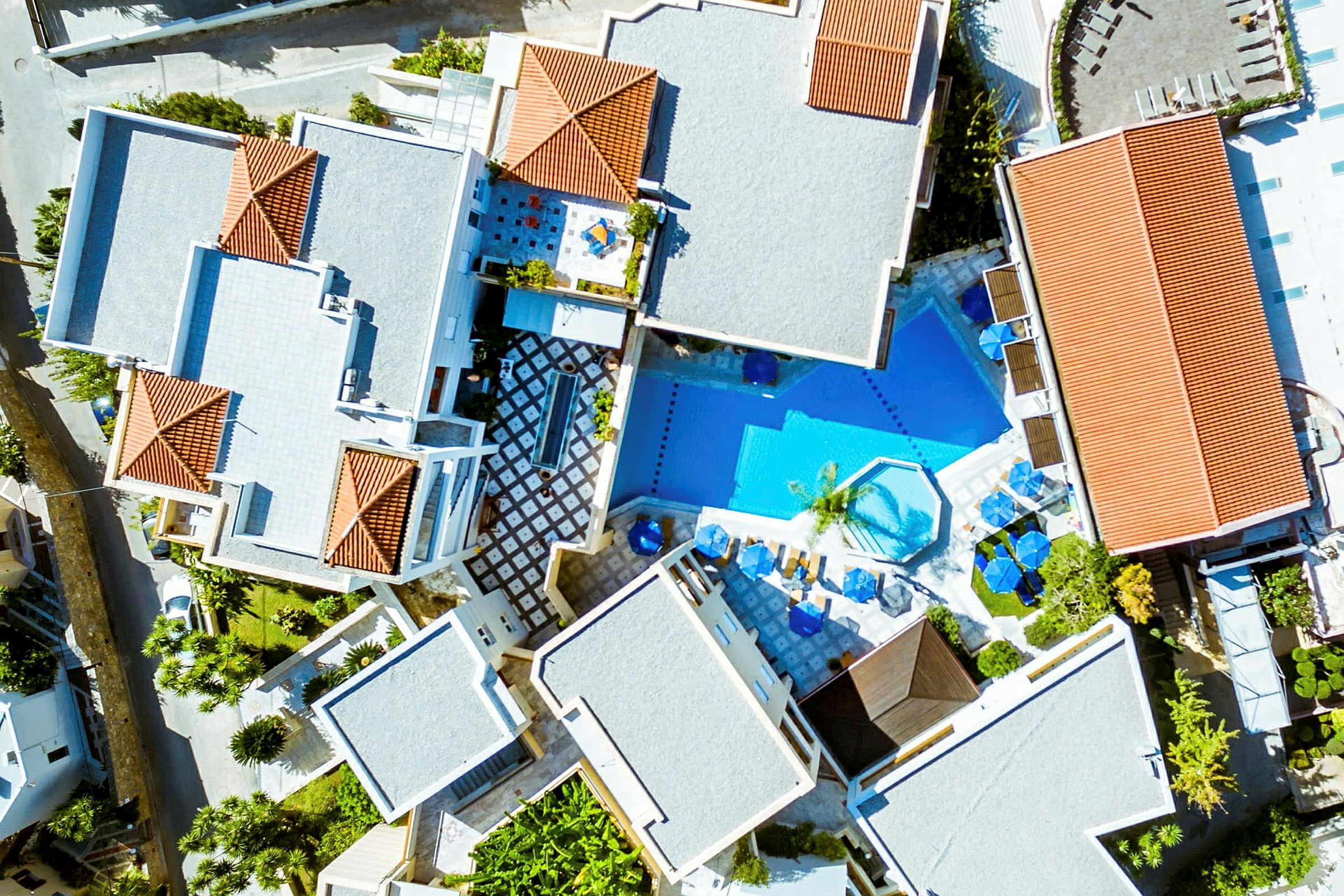Luftfoto af et hotelområde med bygninger og en pool. (AI-genereret tekst)