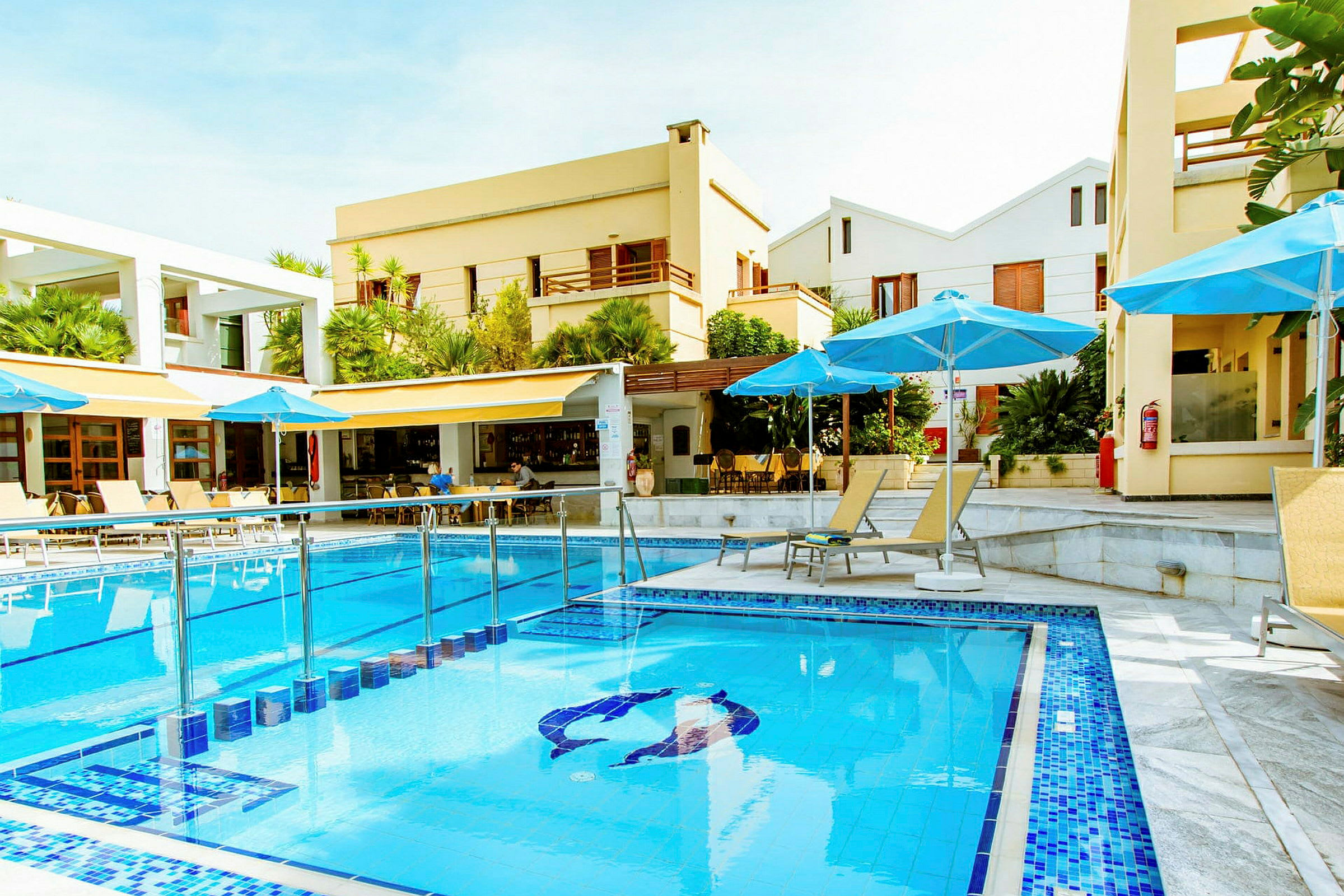 Hotelpool med blåt vand omgivet af liggestole og parasoller. (AI-genereret tekst)
