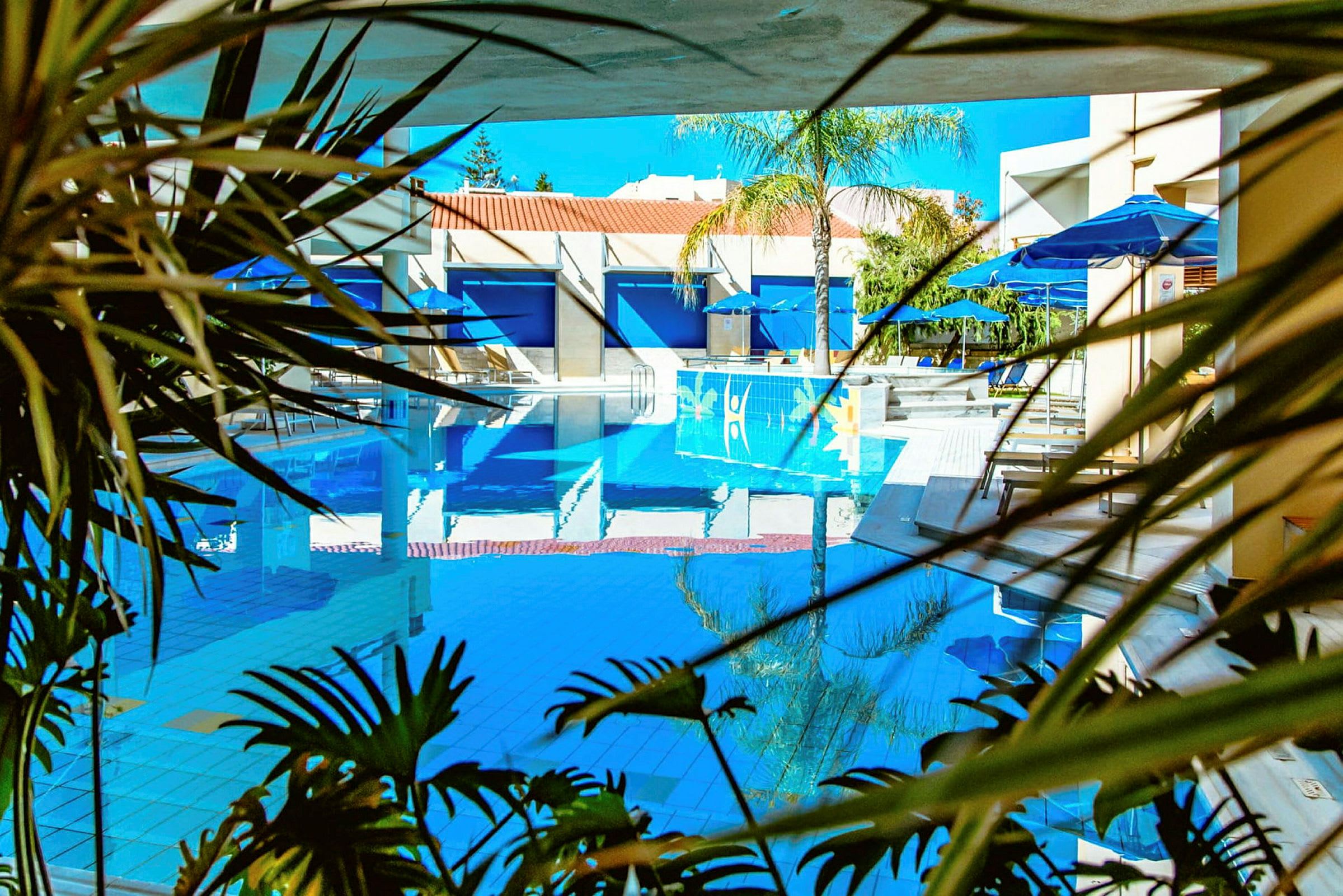 Udendørs pool med liggestole og parasoller i baggrunden, omgivet af tropiske planter. (AI-genereret tekst)