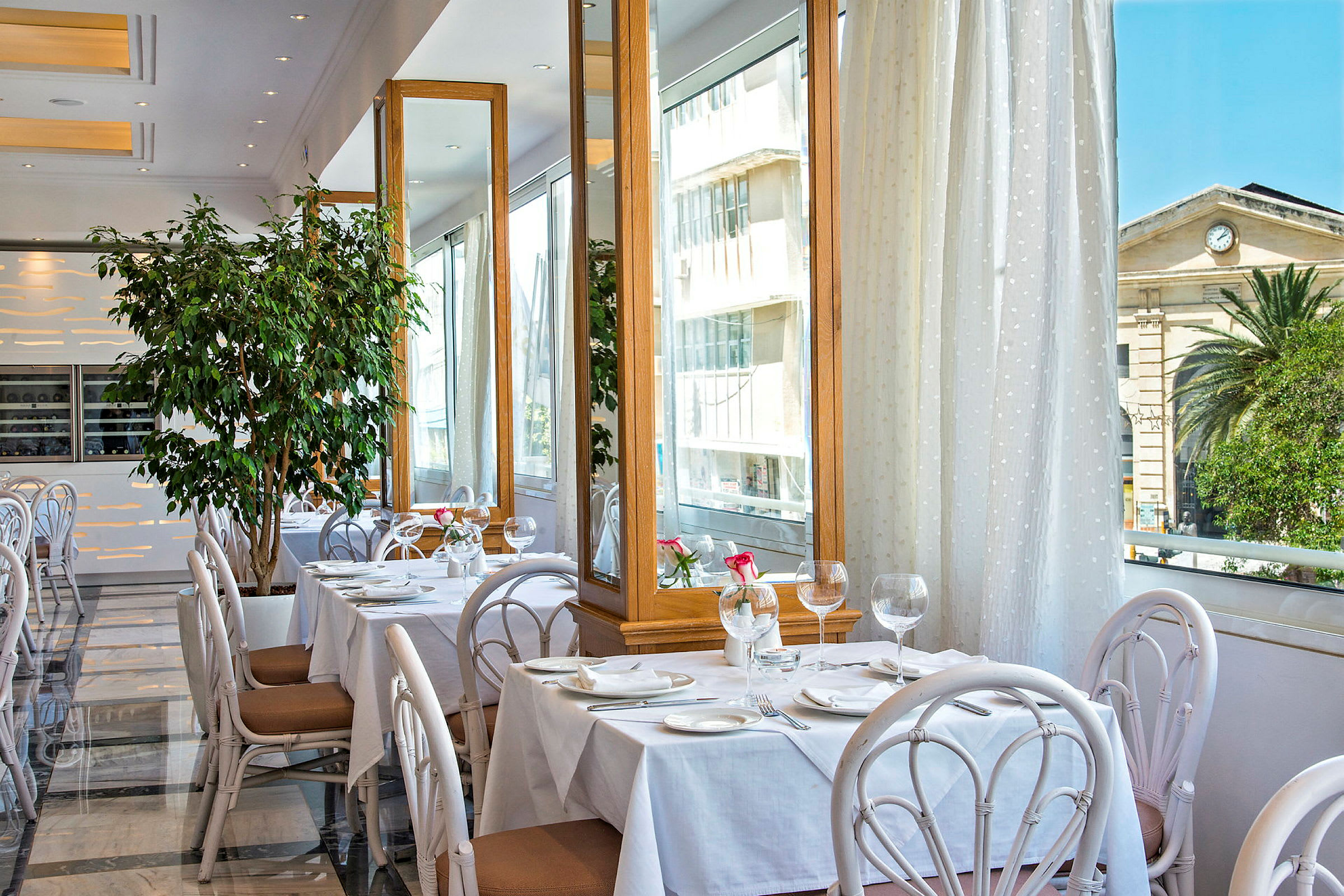 En restaurant med opdækkede borde, store spejle og grønne planter. (AI-genereret tekst)