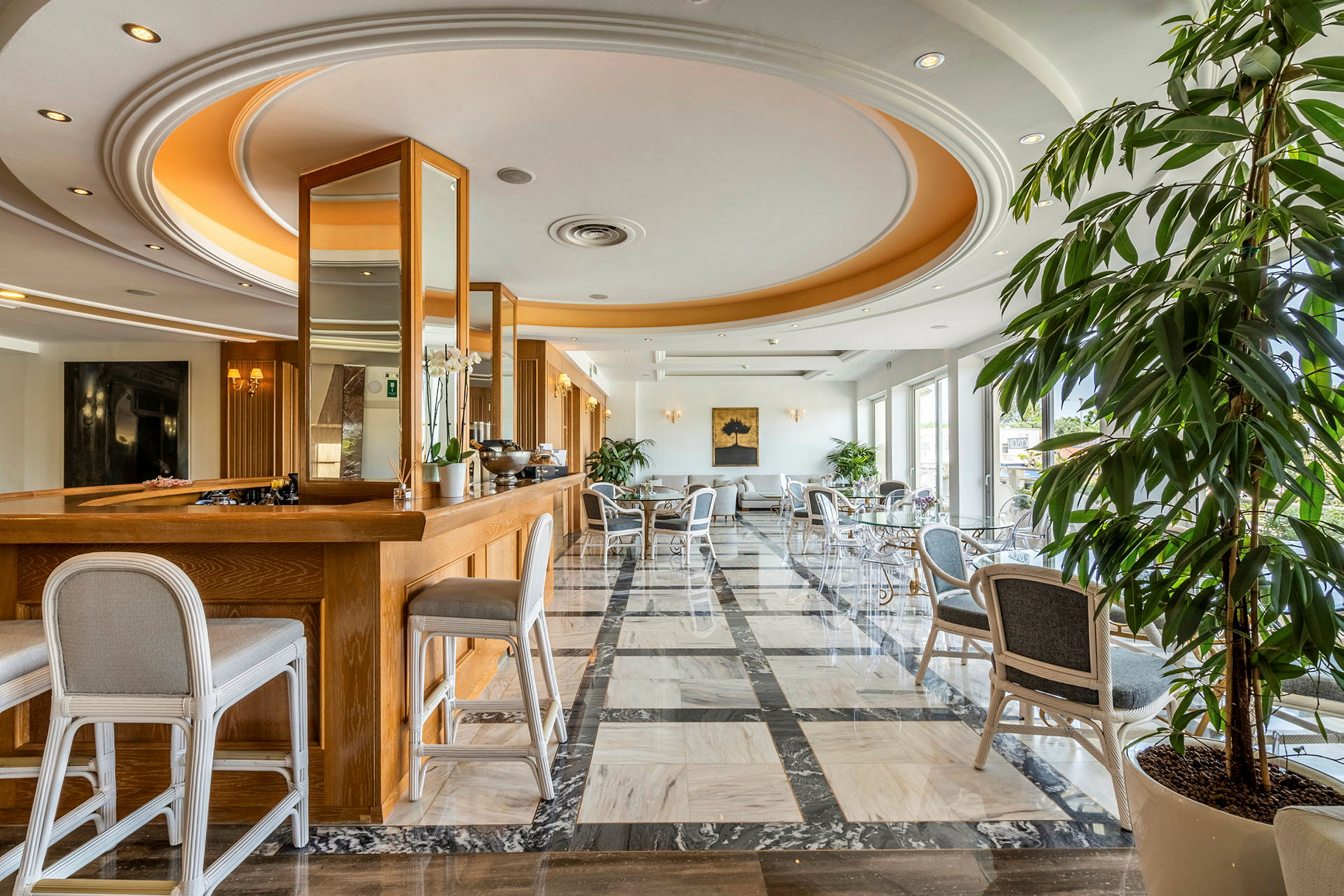 Et elegant hotelværelse med træmøbler og marmorgulv, store vinduer samt planter og siddepladser. (AI-genereret tekst)