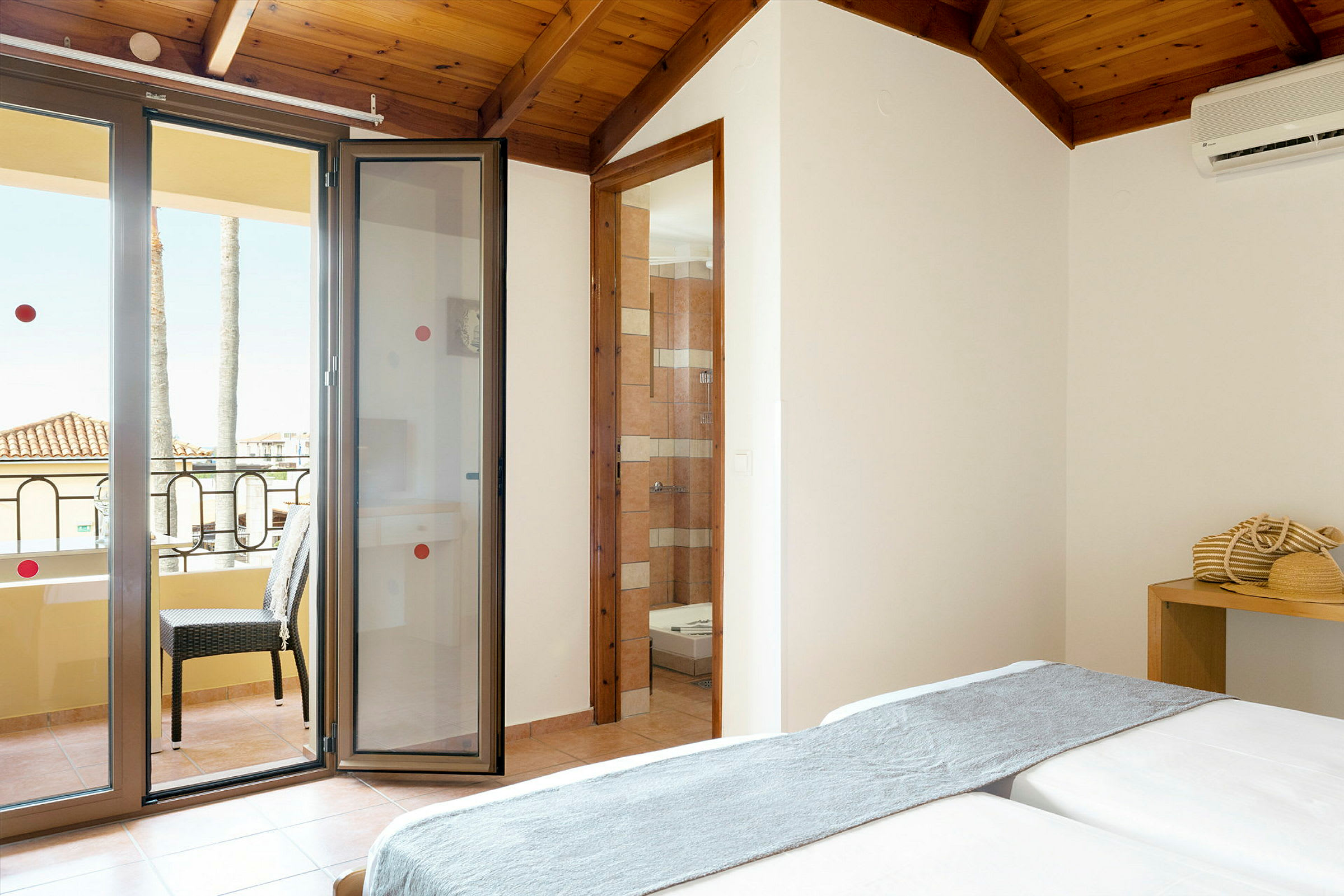 Et hotelværelse med en balkon og åbne døre, samt en siddeplads og en mindre indretningsdetalje. (AI-genereret tekst)