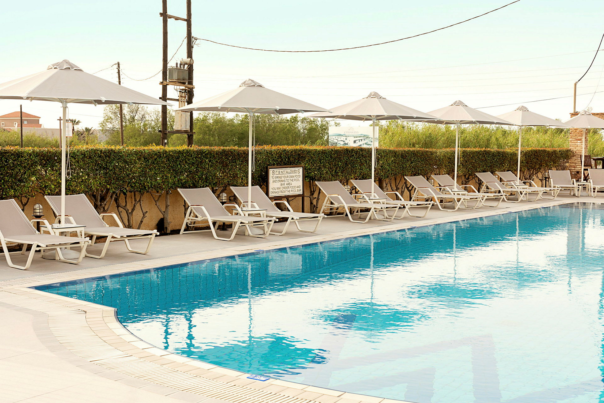 Udendørs swimmingpool med liggestole og parasoller ved siden af. (AI-genereret tekst)