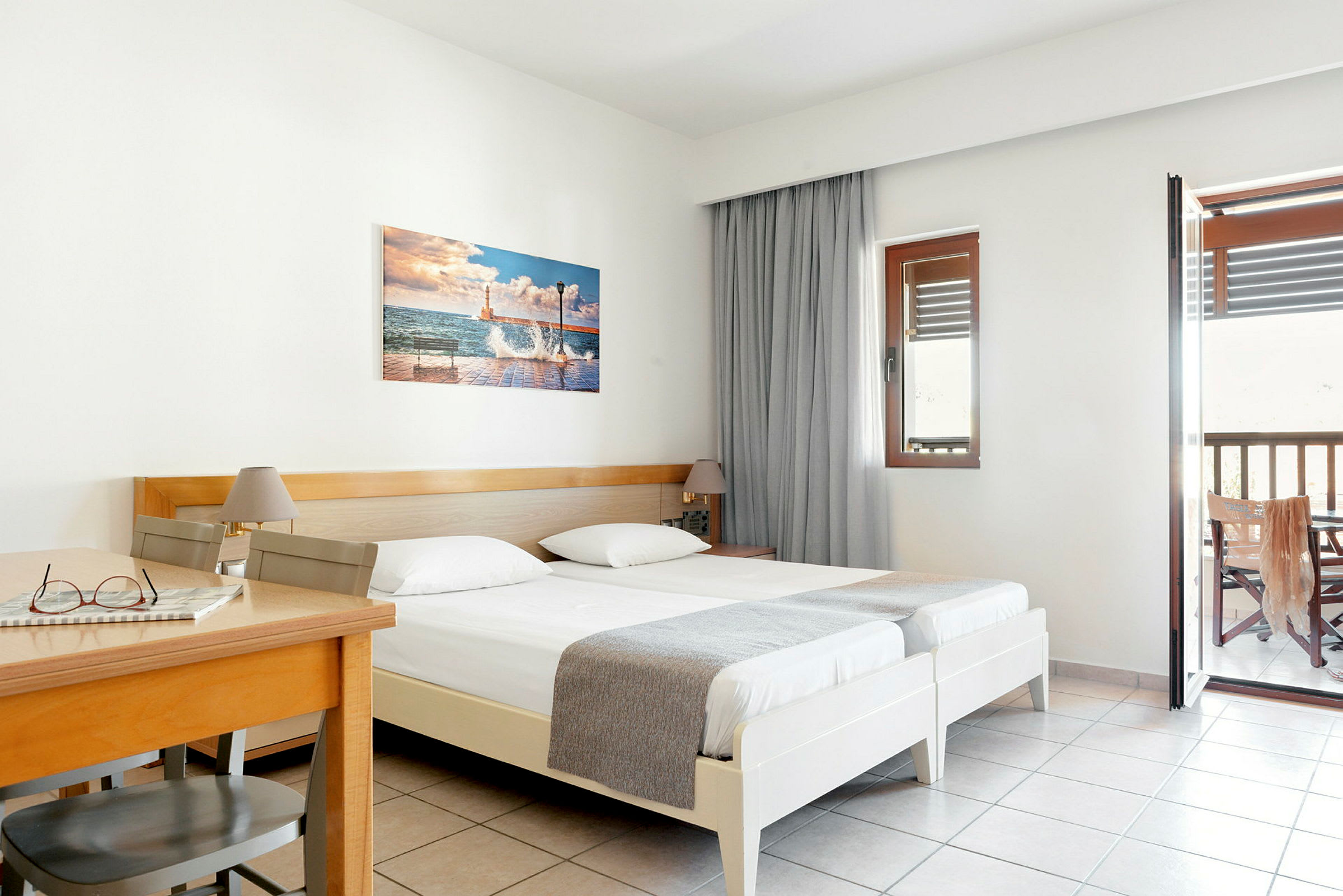 Hotelværelse med to enkeltsenge, et træbord og stol samt altan. (AI-genereret tekst)