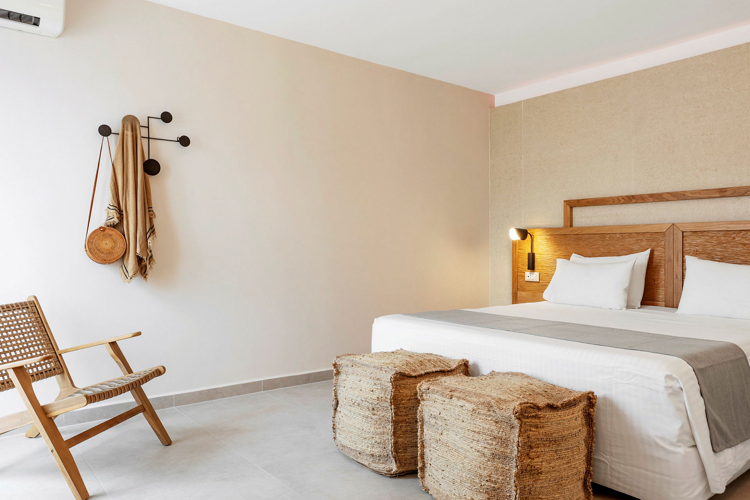Hotelværelse med moderne indretning, inklusive en seng, to afføringsskamler, en stol og en krog på væggen. (AI-genereret tekst)