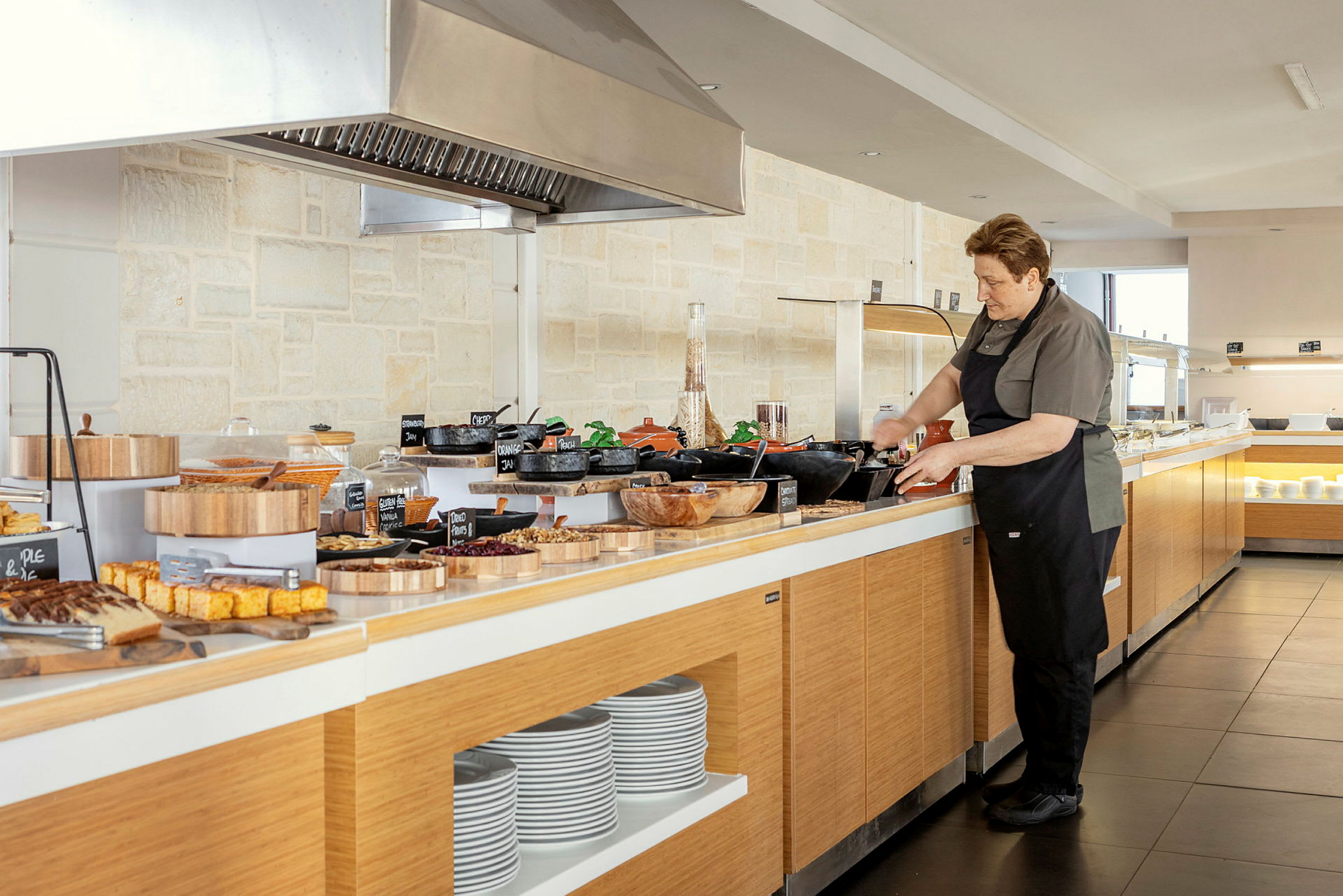 En person står ved en buffet med forskellige retter og tallerkener. (AI-genereret tekst)