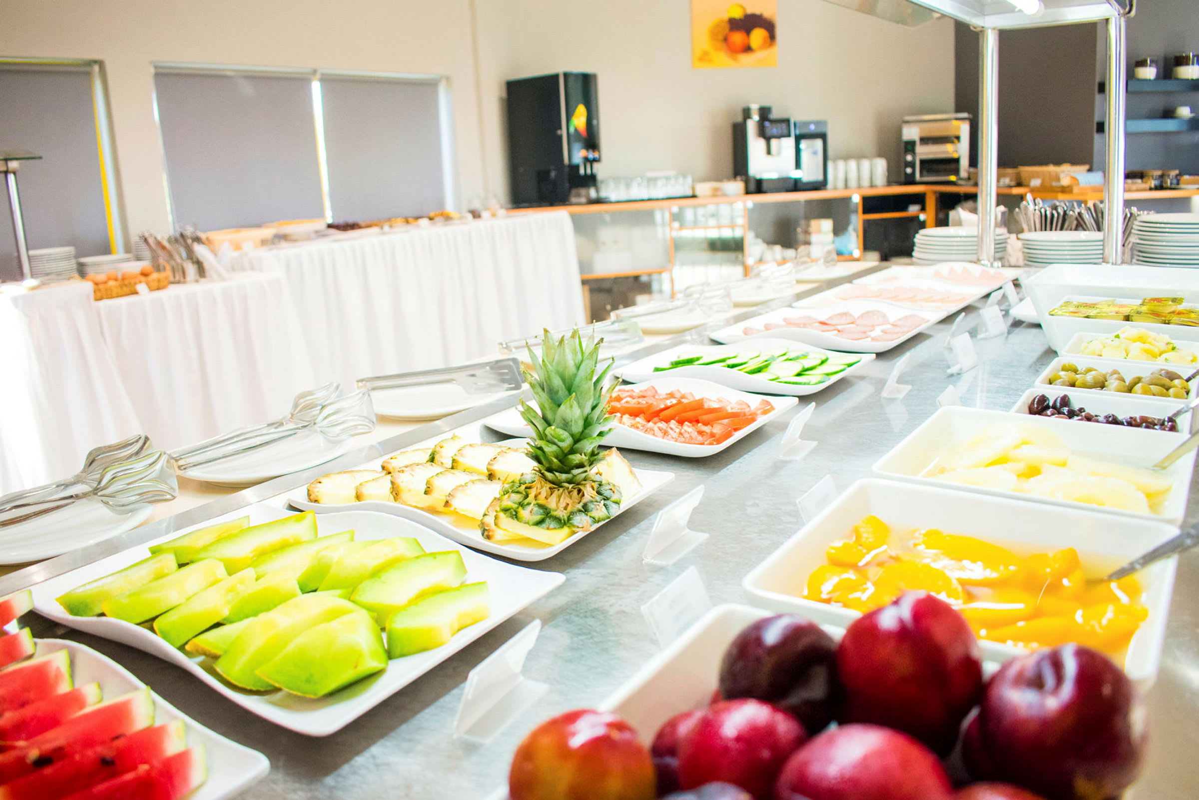 En buffet med forskellige retter, herunder frugt, grøntsager og andre fødevarer, præsenteres i hvide serveringsfade. (AI-genereret tekst)