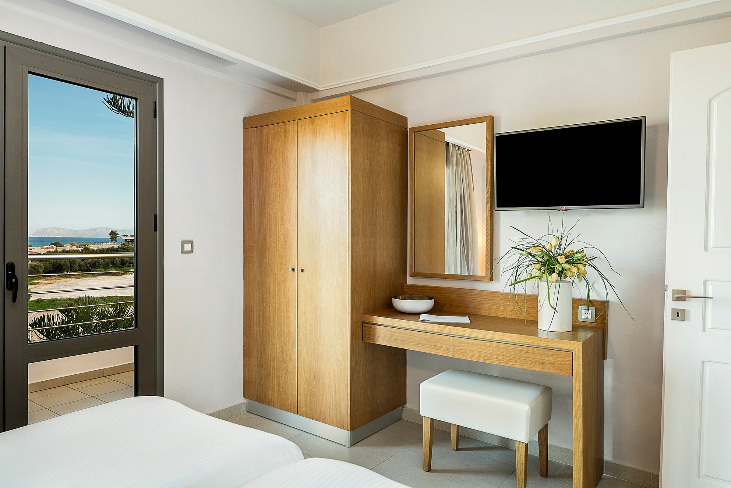 Hotelværelse med garderobe, skrivebord og blomsterdekoration samt udsigt til landskab gennem glasdør. (AI-genereret tekst)