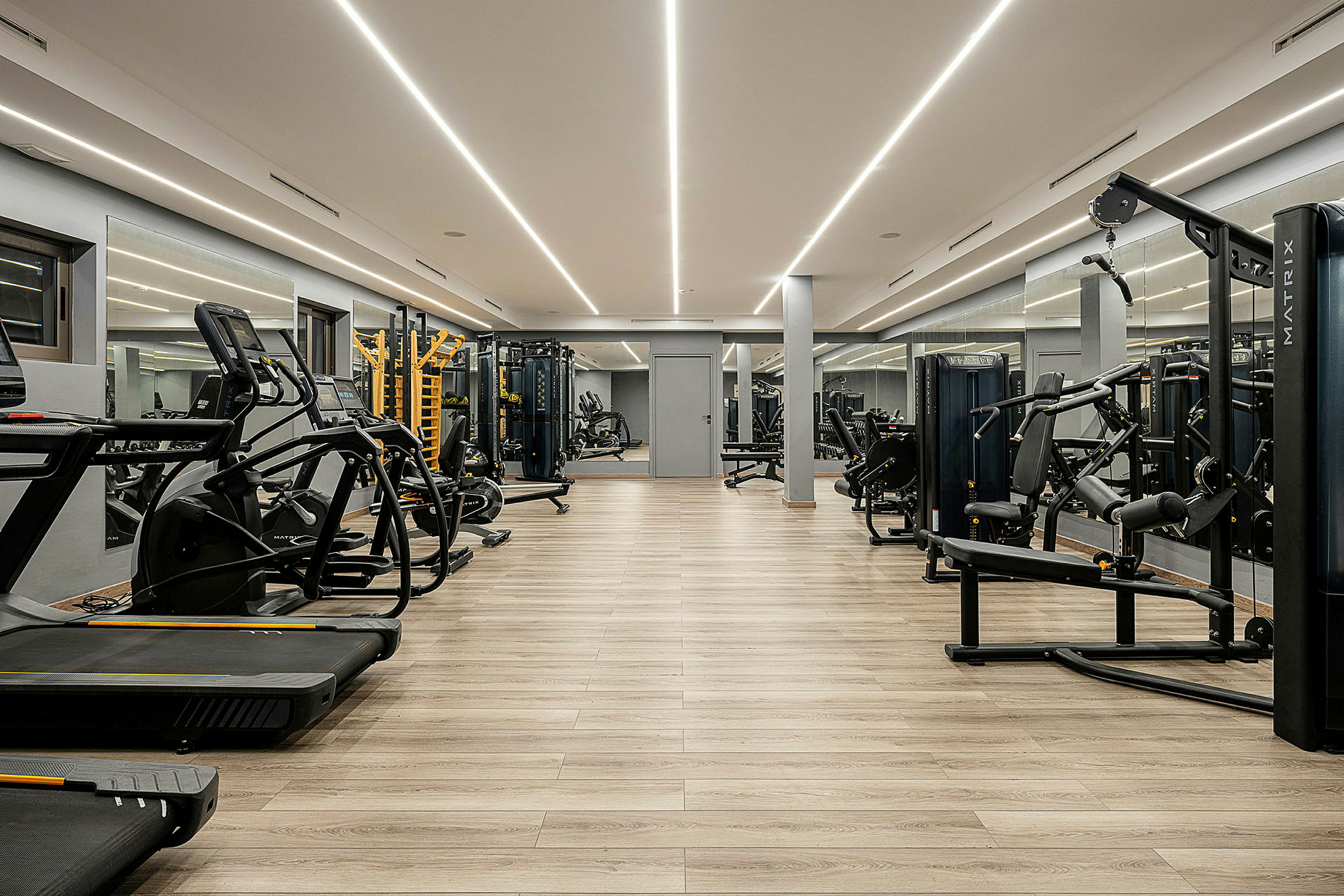 Et moderne fitnesscenter med træningsudstyr, herunder løbebånd og styrketræningsmaskiner, med trægulve og spejle langs væggene. (AI-genereret tekst)