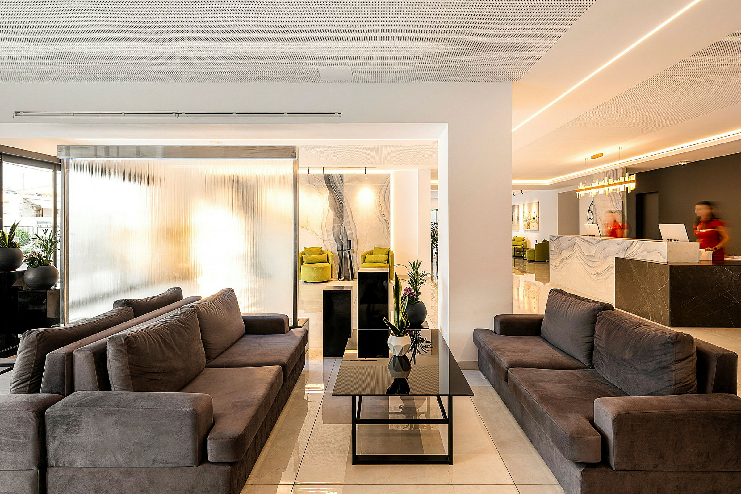 En moderne hotellobby med komfortable sofaer, et glasbord og receptionen i baggrunden. (AI-genereret tekst)
