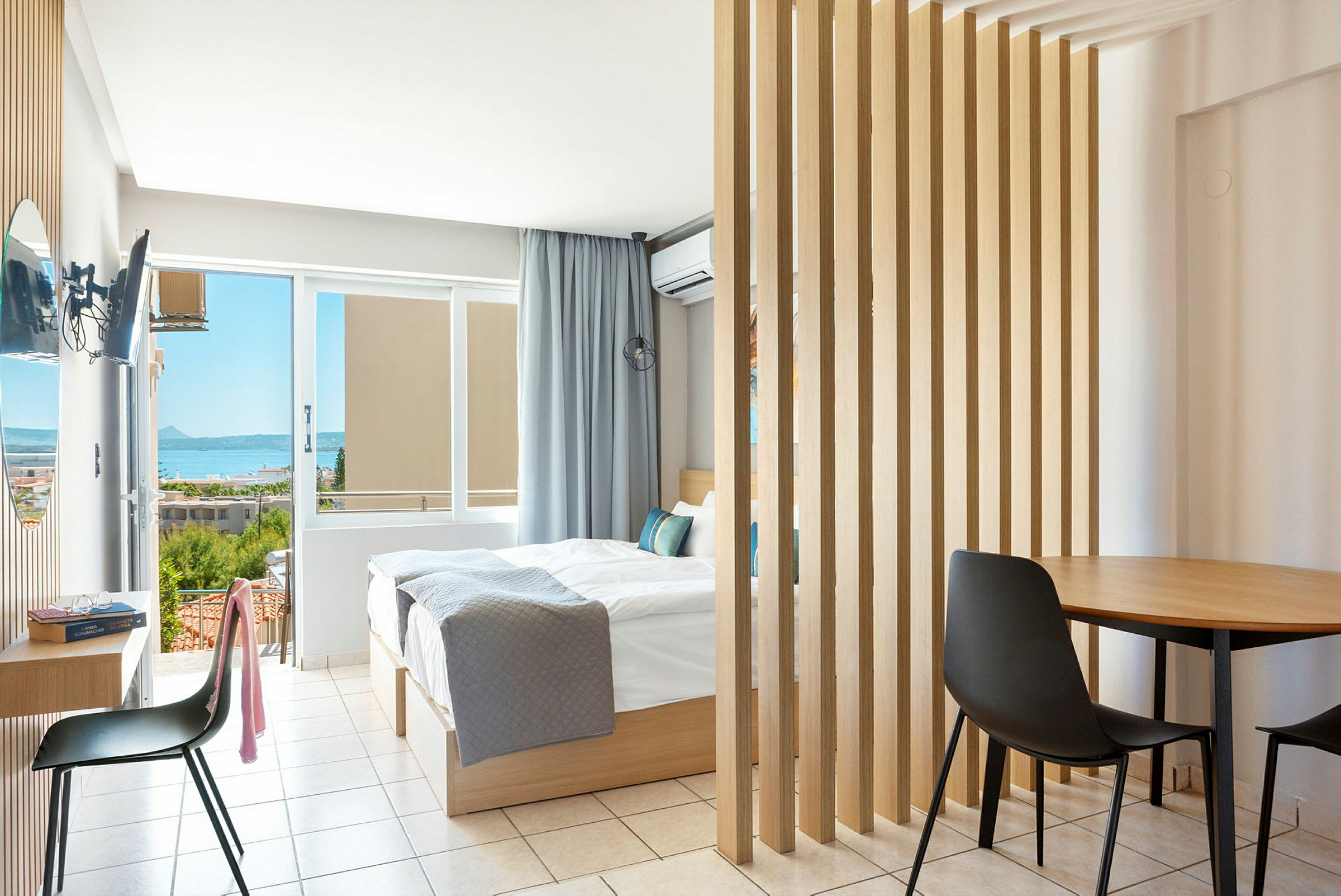 Et lyst hotelværelse med dobbeltseng og udsigt over havet. (AI-genereret tekst)