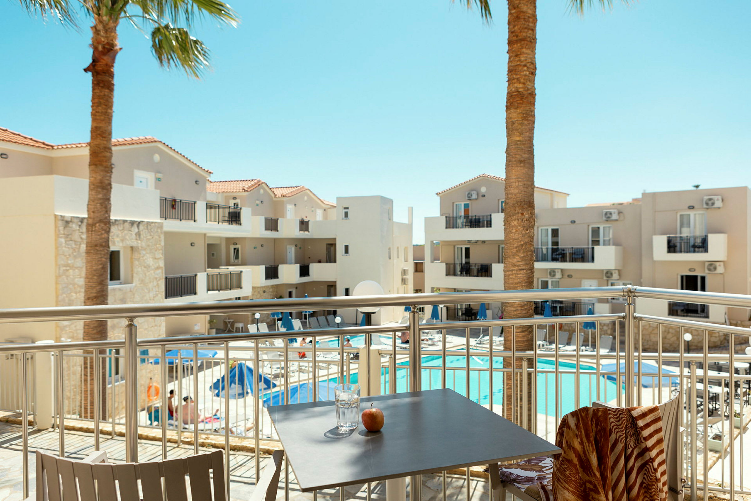Hotelbygning med altaner og pool, set fra en terrasse. (AI-genereret tekst)