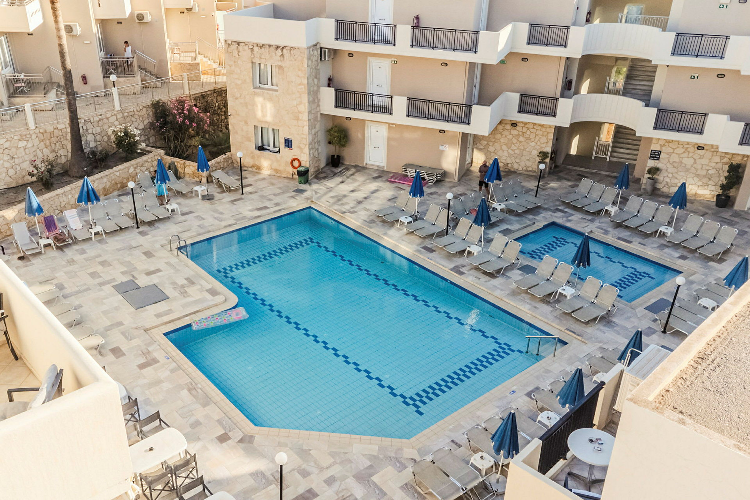 Udendørs swimmingpool med liggestole og parasoller ved en hotelbygning. (AI-genereret tekst)