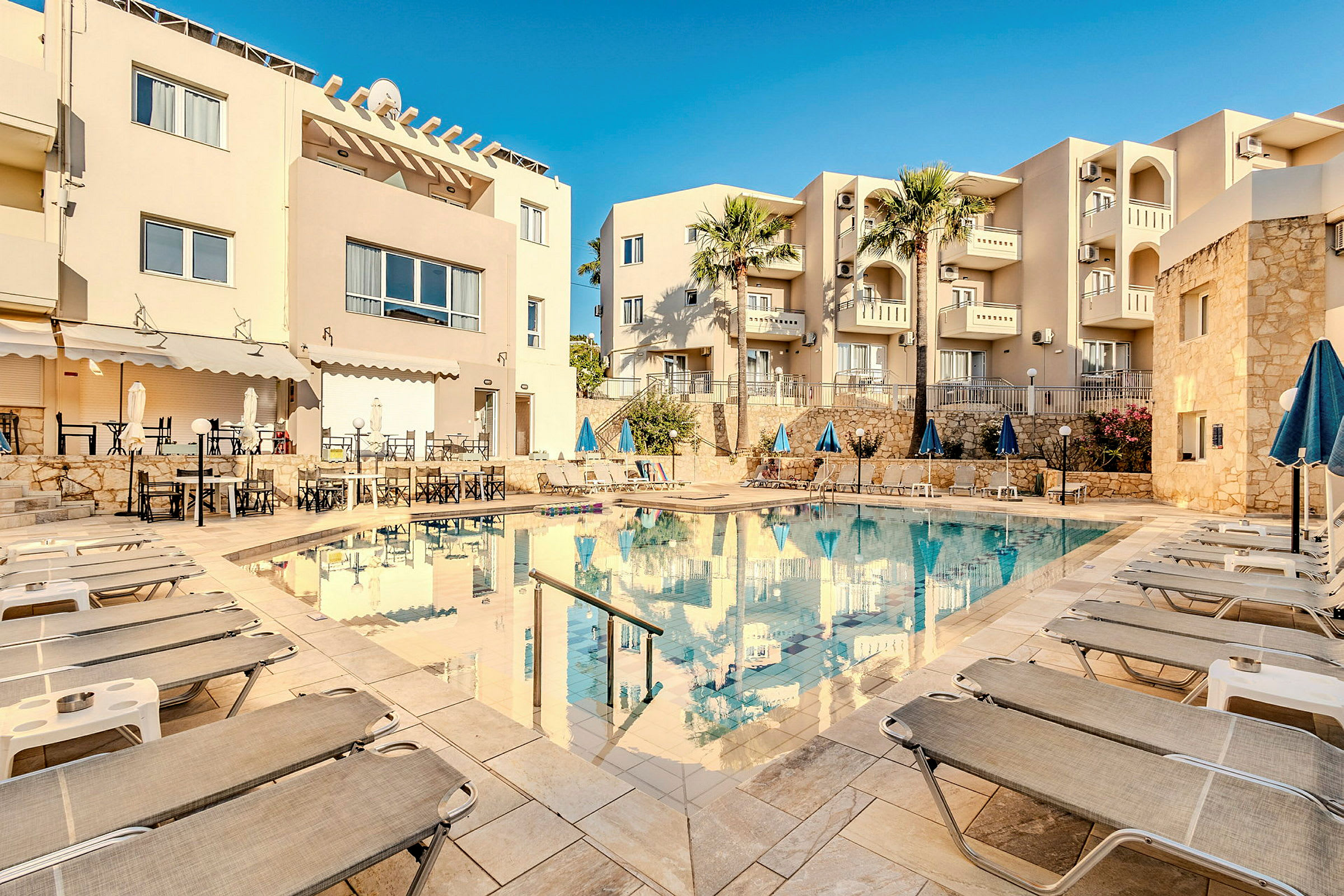 En hotelpool omgivet af liggestole og bygninger. (AI-genereret tekst)