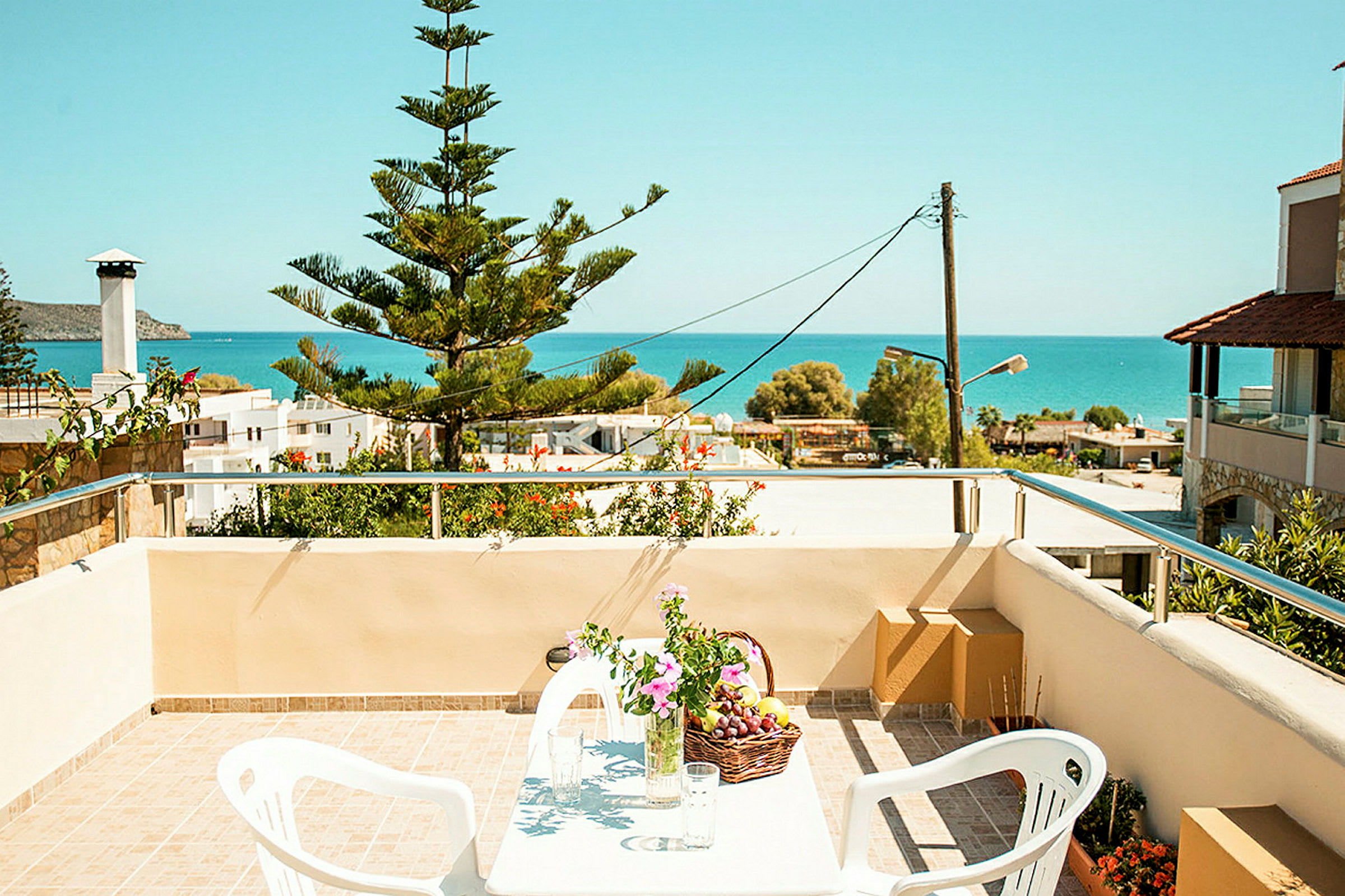 Udsigt fra en terrasse med bord, stole og blomster mod havet. (AI-genereret tekst)