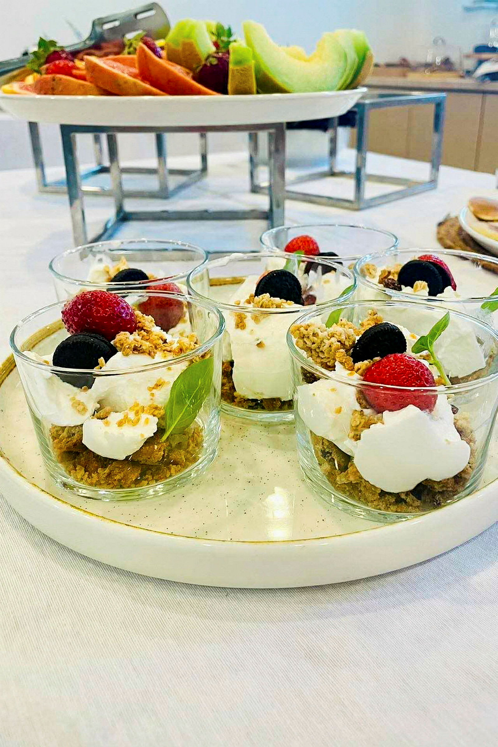 Fire glas med dessert, pyntet med friske bær og sprø topping, på en lys tallerken. (AI-genereret tekst)