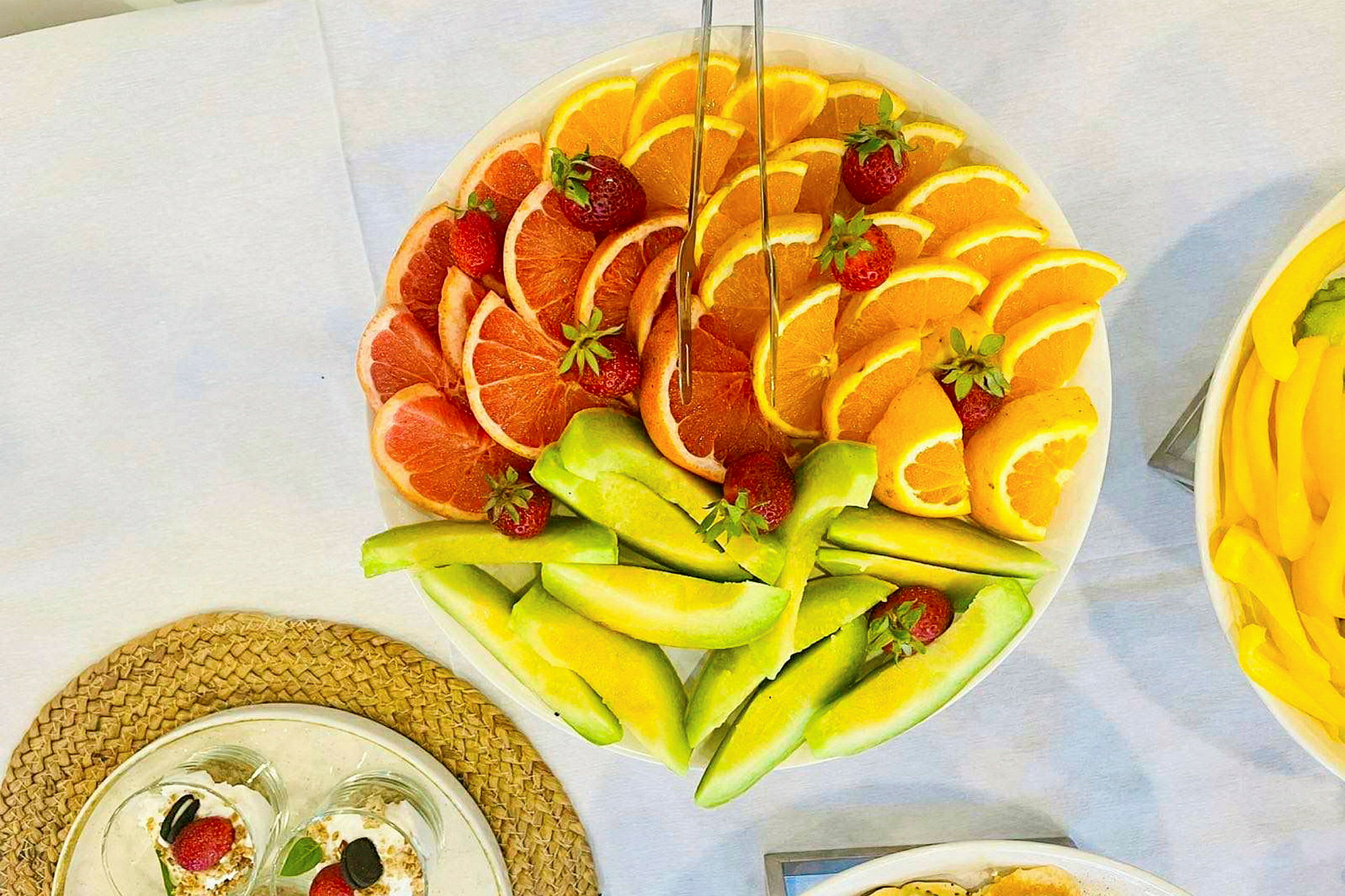 En tallerken med skåret frugt som grapefrugt, appelsiner og melon, dekoreret med jordbær. (AI-genereret tekst)