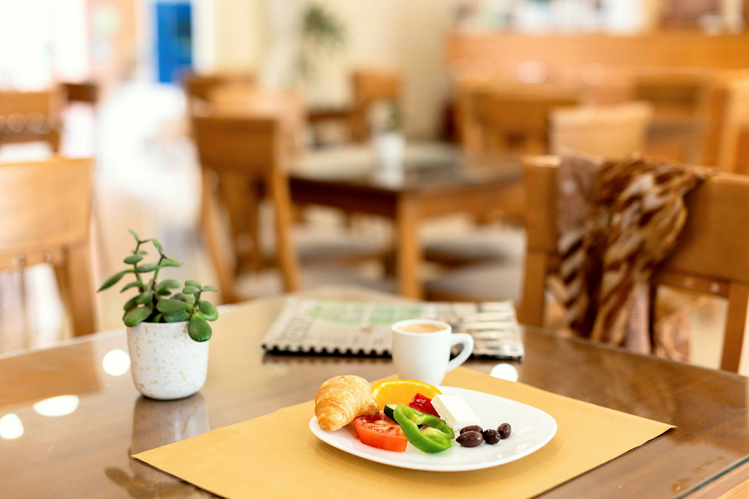 En tallerken med morgenmad bestående af croissant, grøntsager og kaffe på et bord med dekorationer. (AI-genereret tekst)