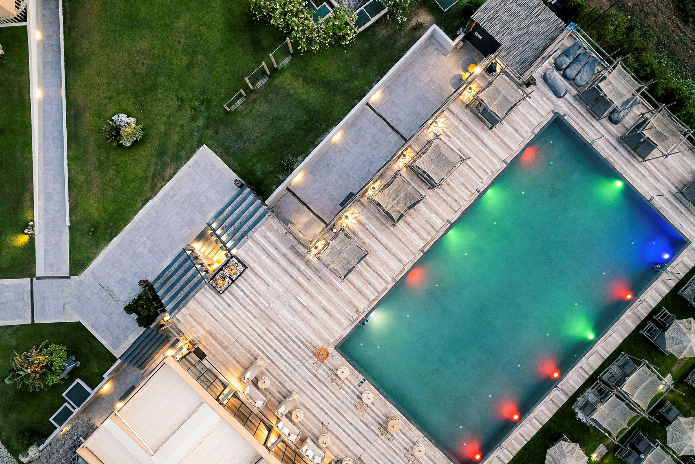 Luftfoto af en udendørs swimmingpool omgivet af liggestole og grønne omgivelser. (AI-genereret tekst)