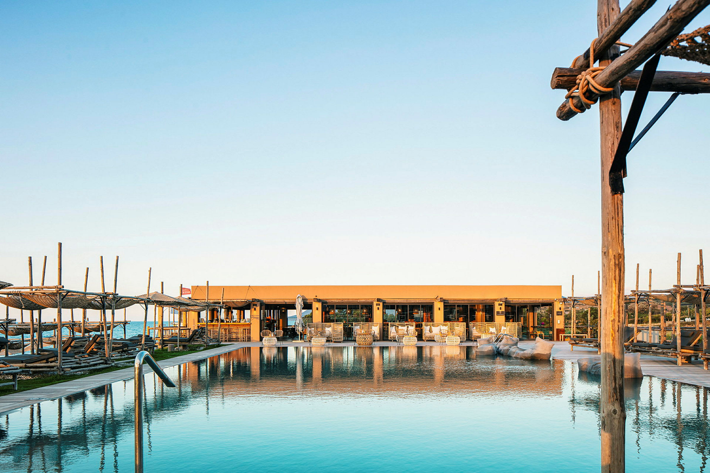 Billede af en pool med liggestole og et hus i baggrunden ved solopgang eller solnedgang. (AI-genereret tekst)