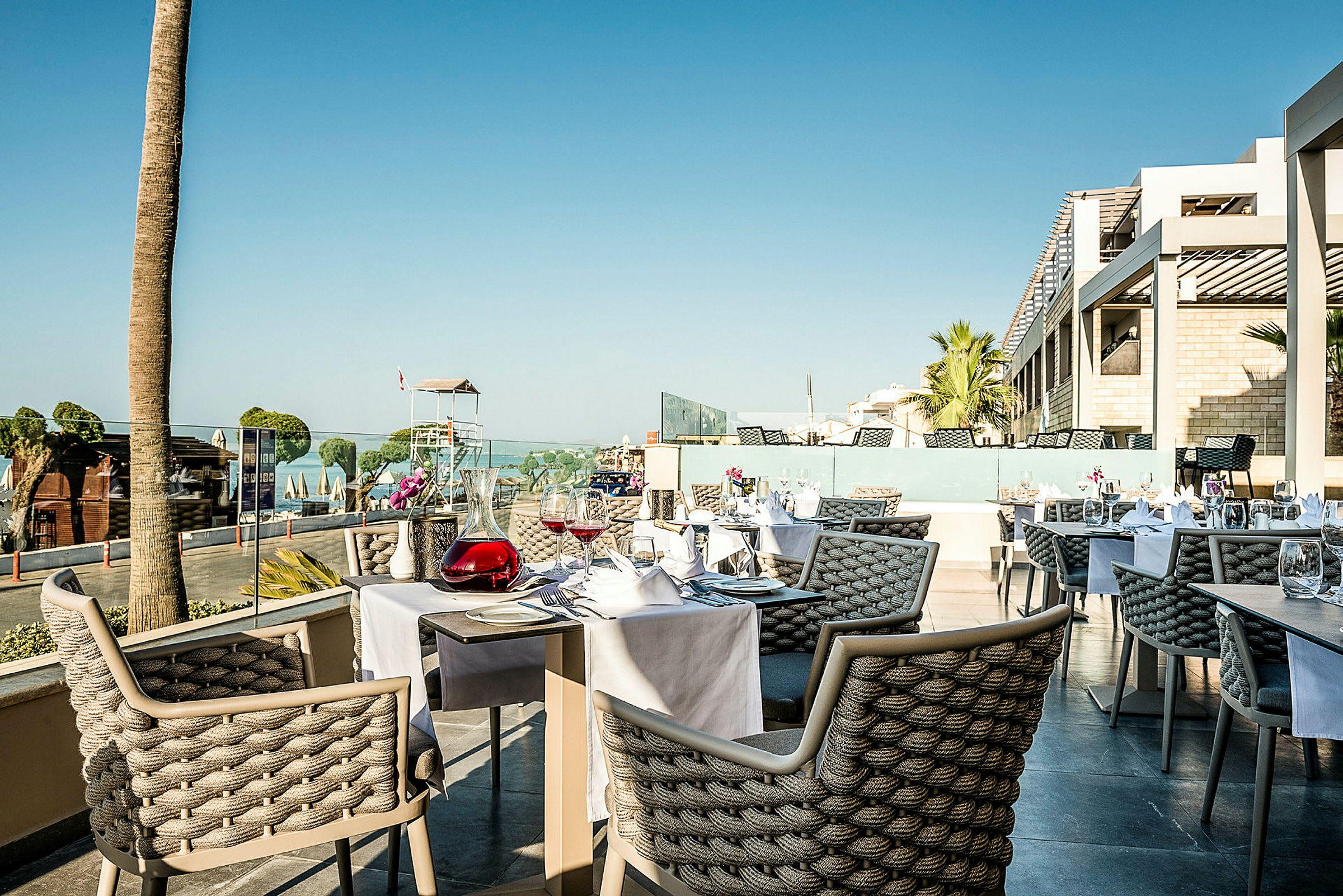 Udendørsrestaurant med dækkede borde og udsigt over strand og hav. (AI-genereret tekst)