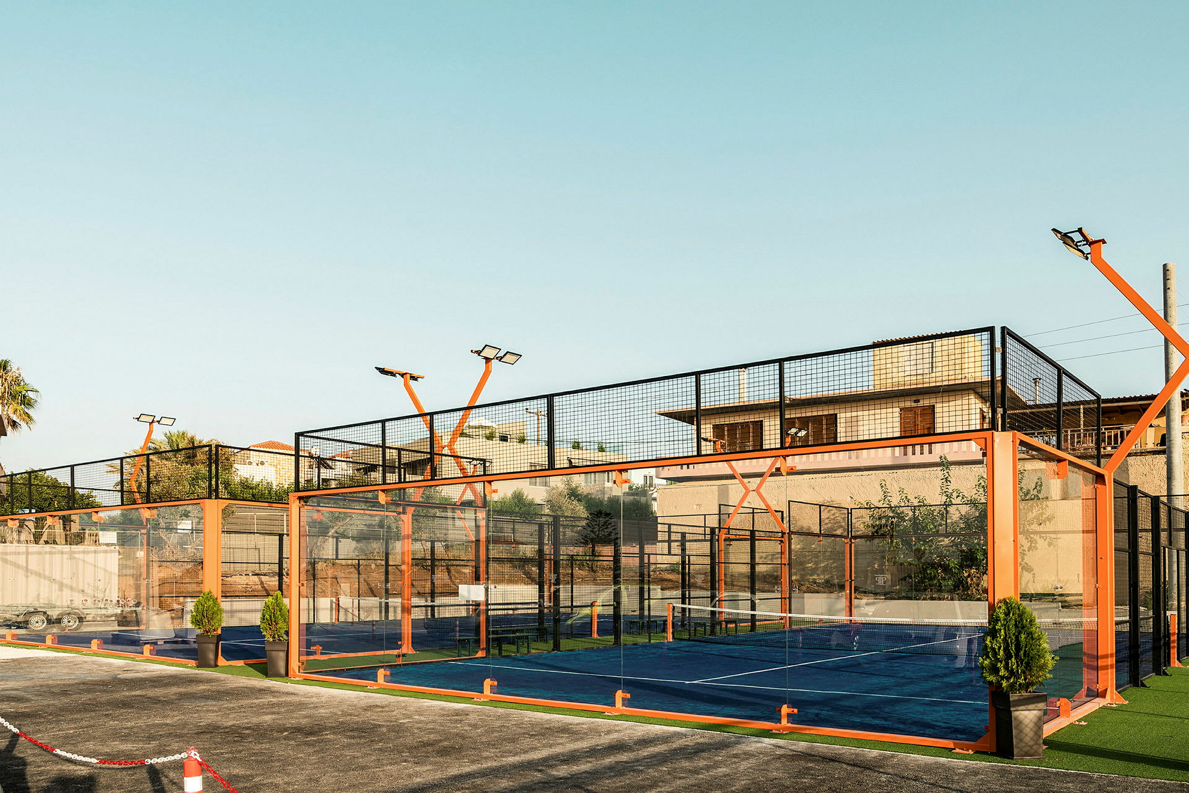 Udendørs padelbane omgivet af net og orange struktur, ved solnedgang. (AI-genereret tekst)