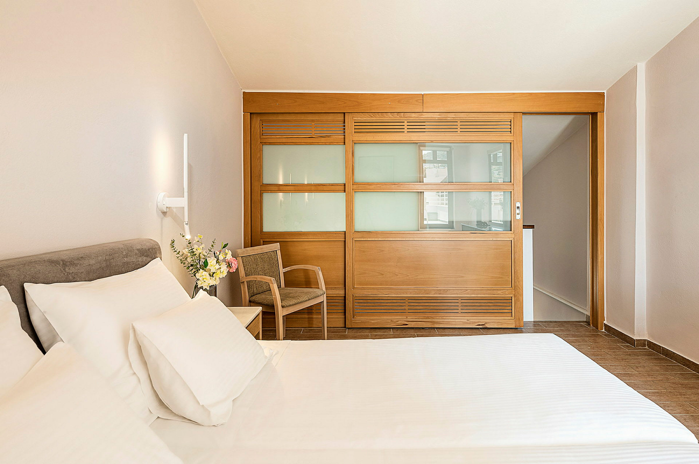 Hotelværelse med seng, stol og en træpanel med glas. (AI-genereret tekst)