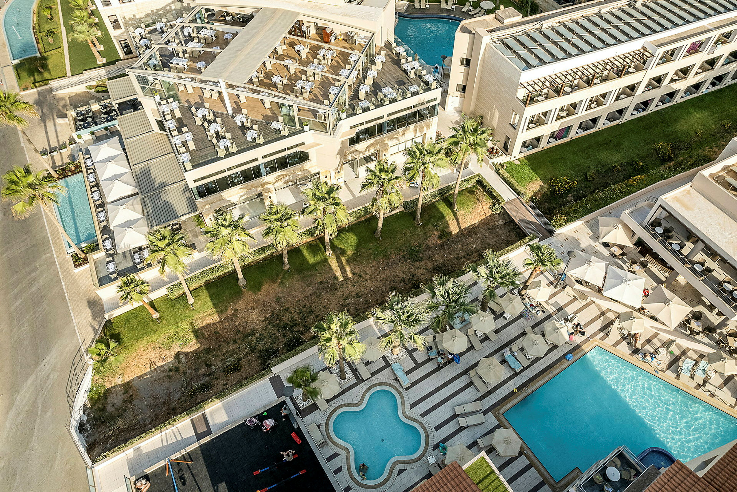 En udsigt over hotelområde med swimmingpools, palmetræer og solsenge. (AI-genereret tekst)