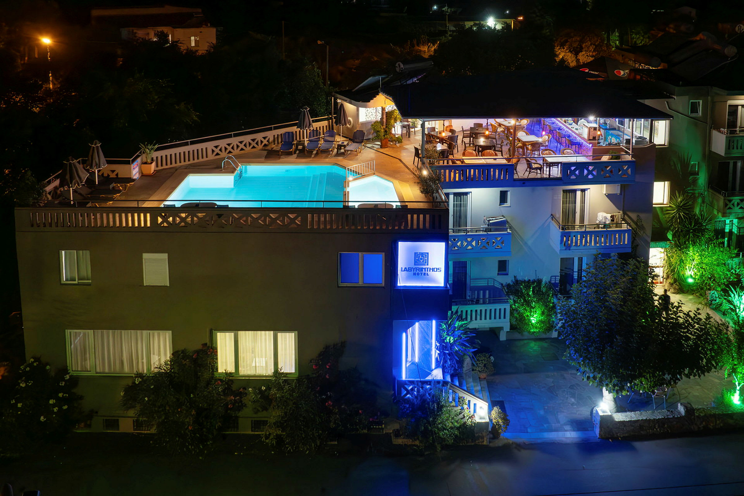 Et hotel med belyst facade og en oplyst udendørs swimmingpool om aftenen. (AI-genereret tekst)