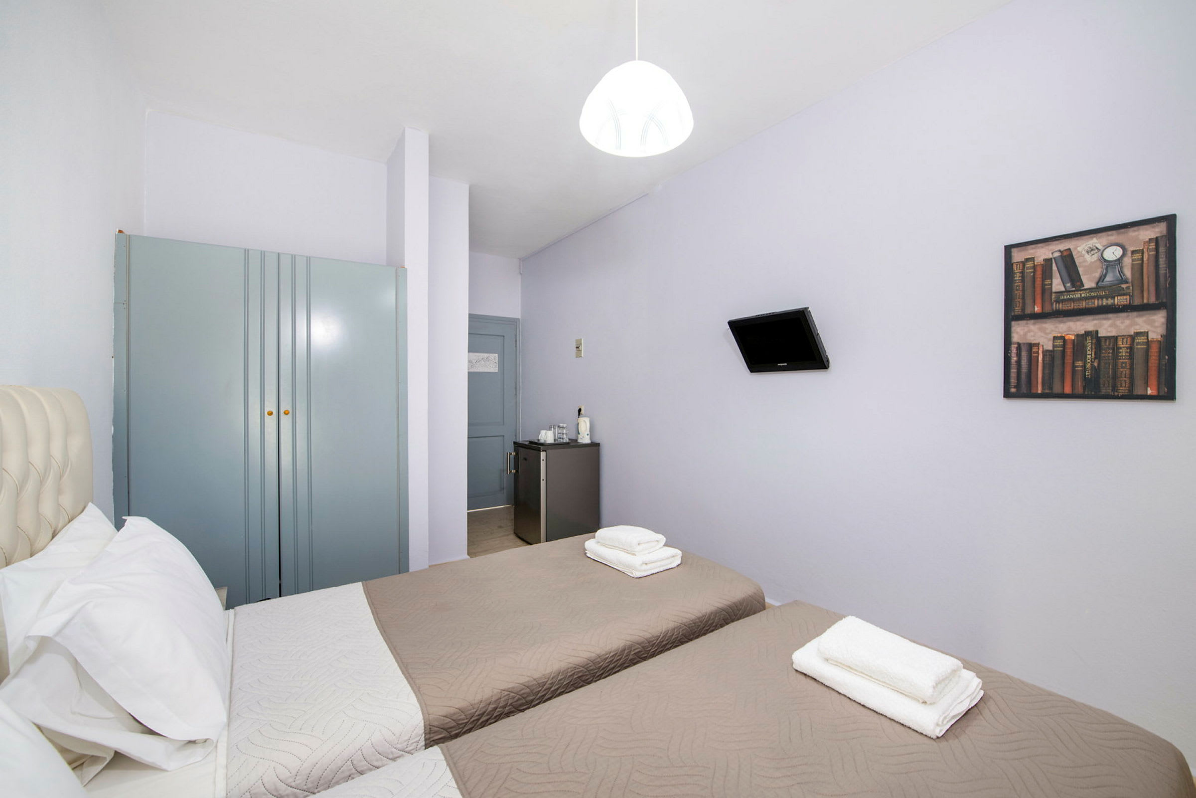 Hotelværelse med to enkeltsenge, et klædeskab, et lille køleskab og et vægmonteret fjernsyn. (AI-genereret tekst)