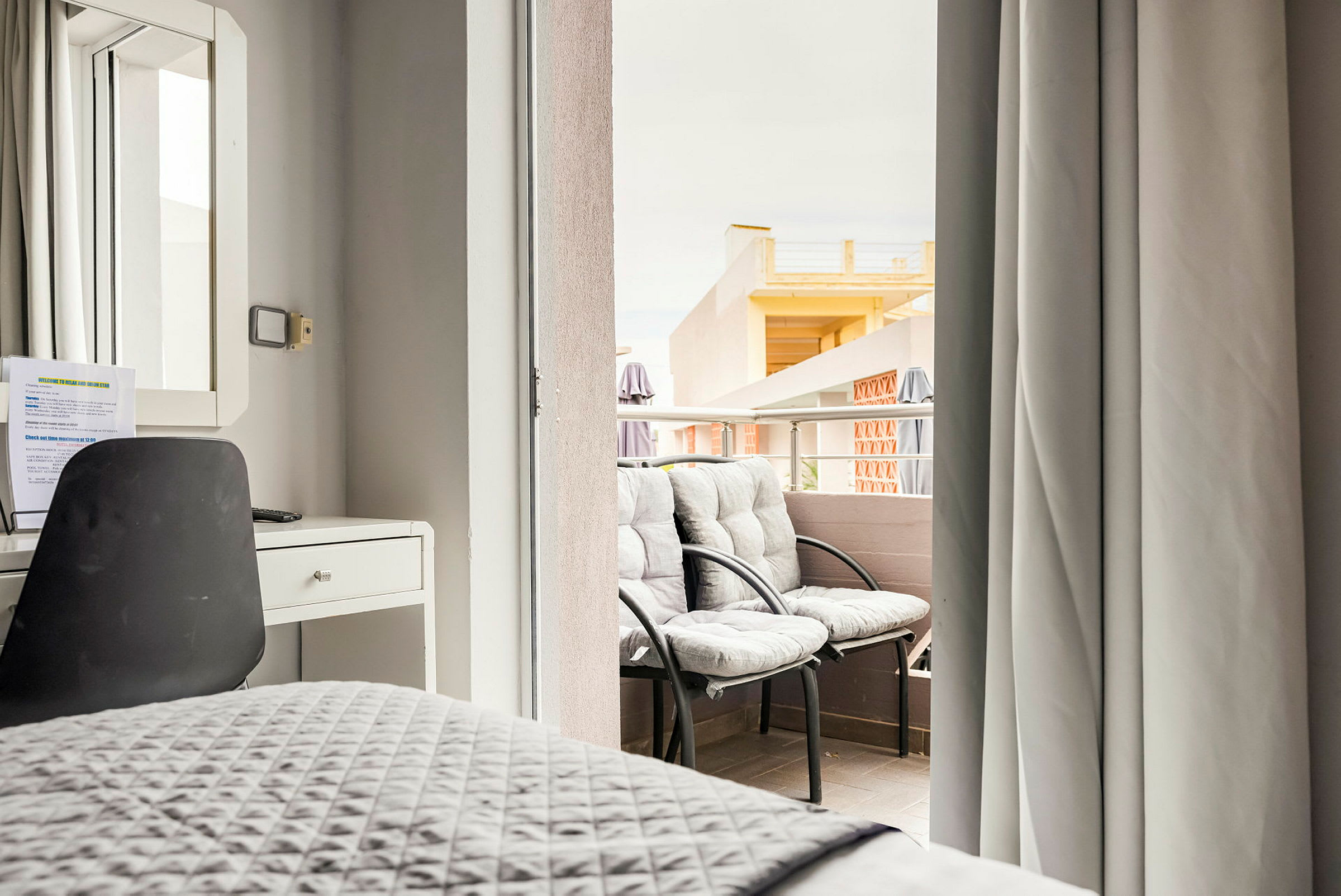 En hotelværelsesindretning med skrivebord og stol og udsigt til en altan med to stole. (AI-genereret tekst)