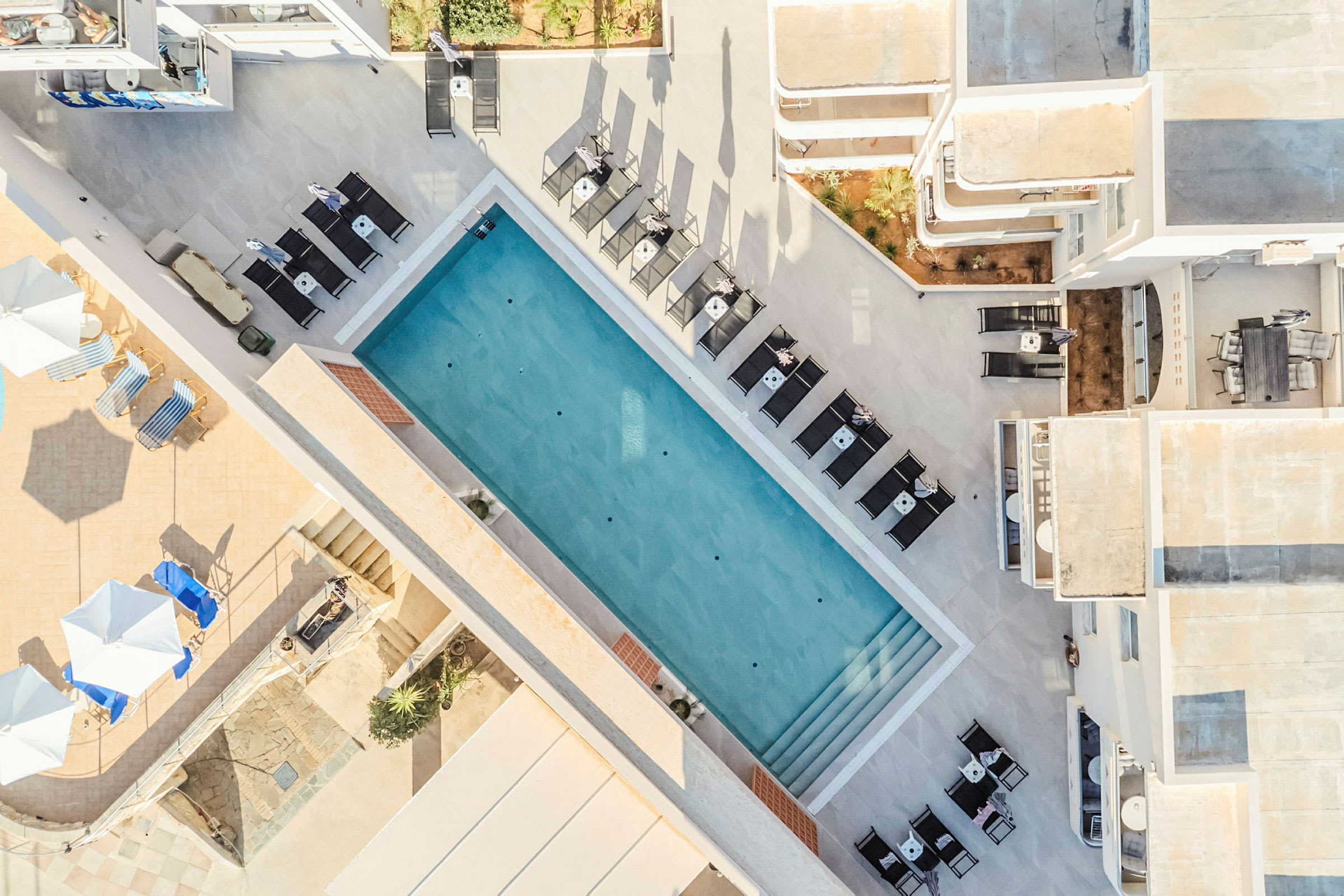 Luftfoto af en udendørs pool omgivet af liggestole og borde. (AI-genereret tekst)