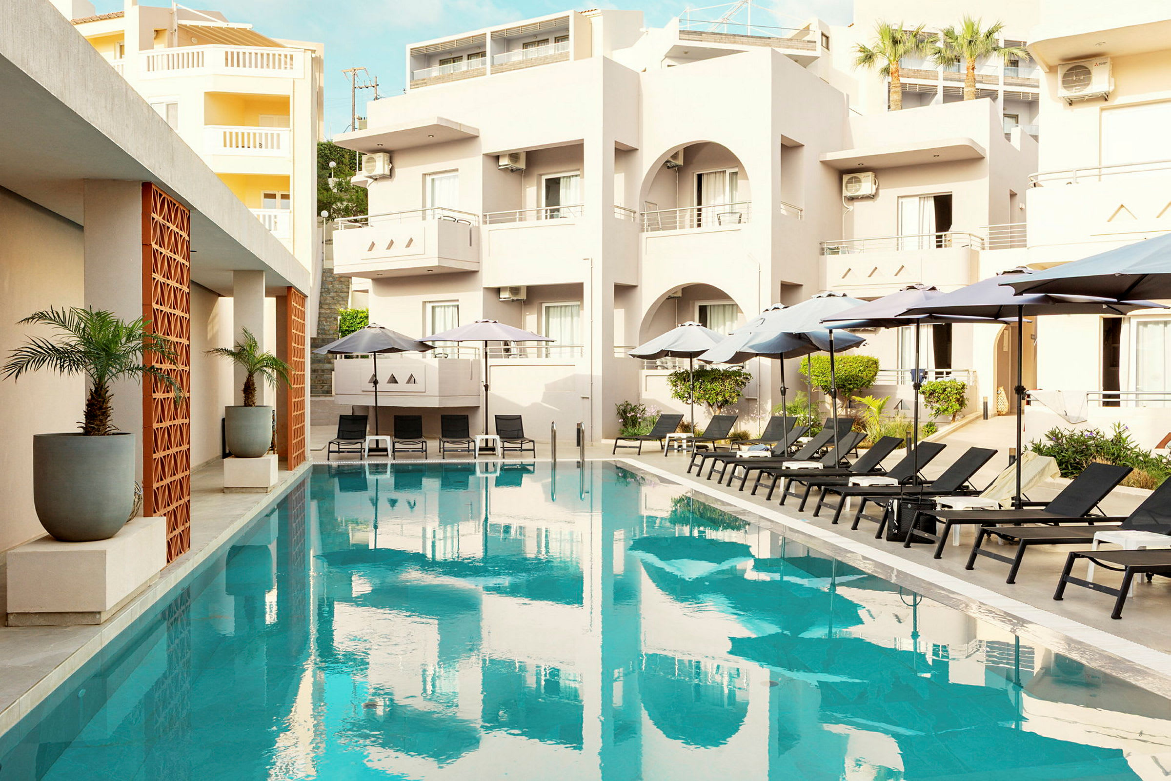 En udendørs pool med liggestole og parasoller ved et hotel. (AI-genereret tekst)