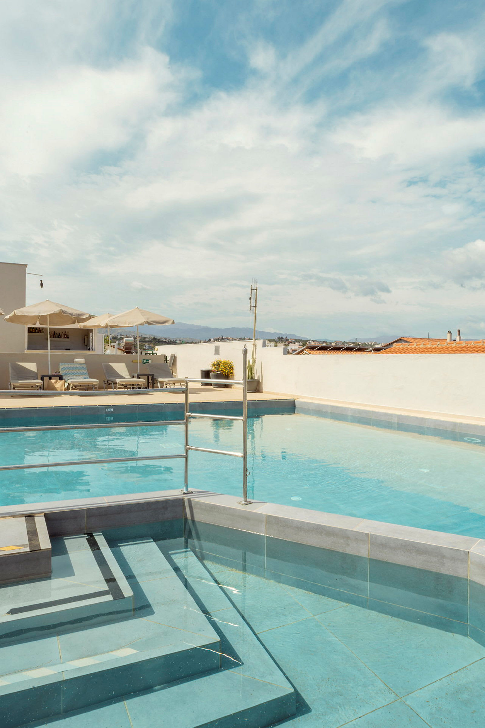 En udendørs pool med liggestole og parasoller under en klar himmel. (AI-genereret tekst)