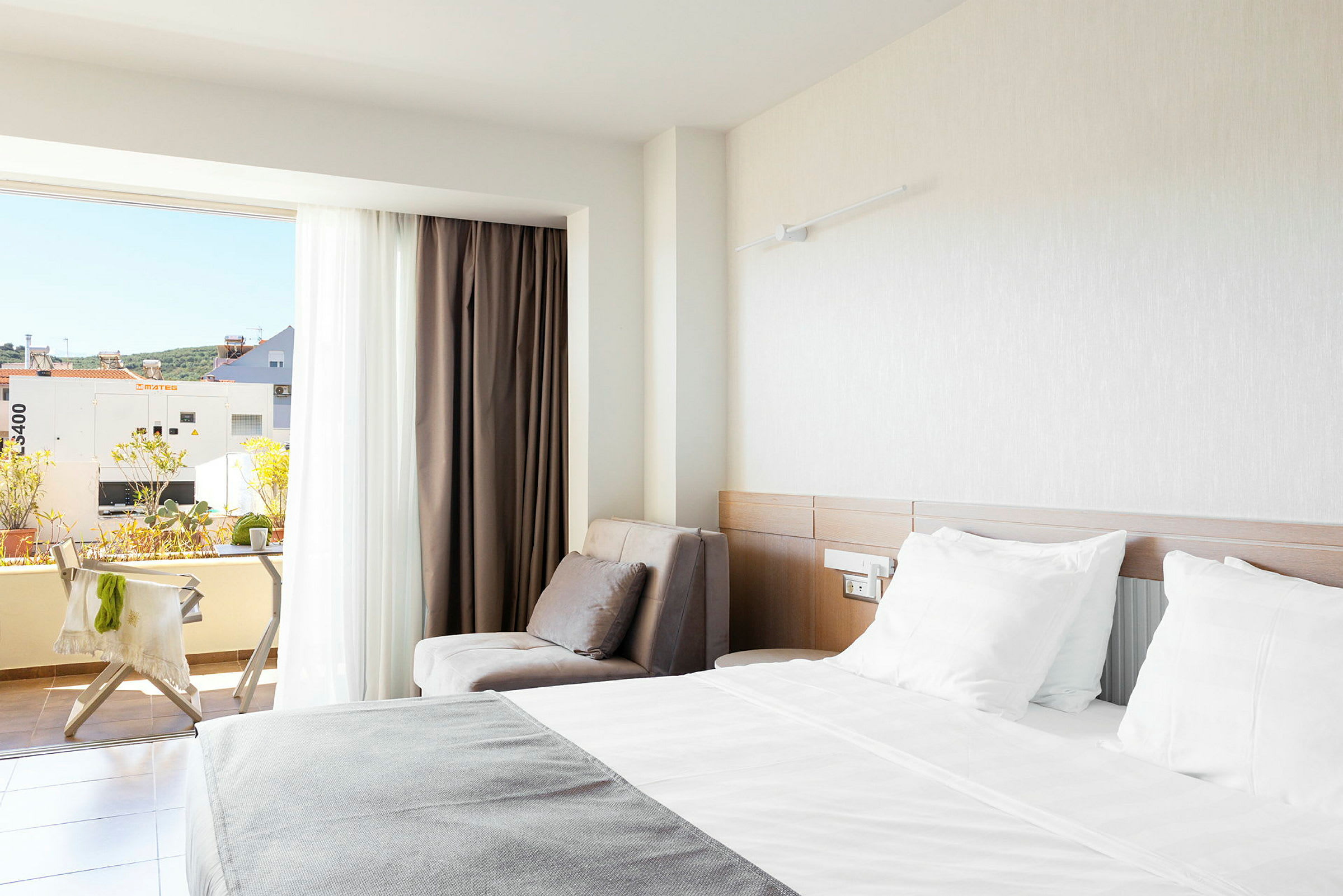 Et hotelværelse med en dobbeltseng, en lænestol og en balkon med udsigt. (AI-genereret tekst)