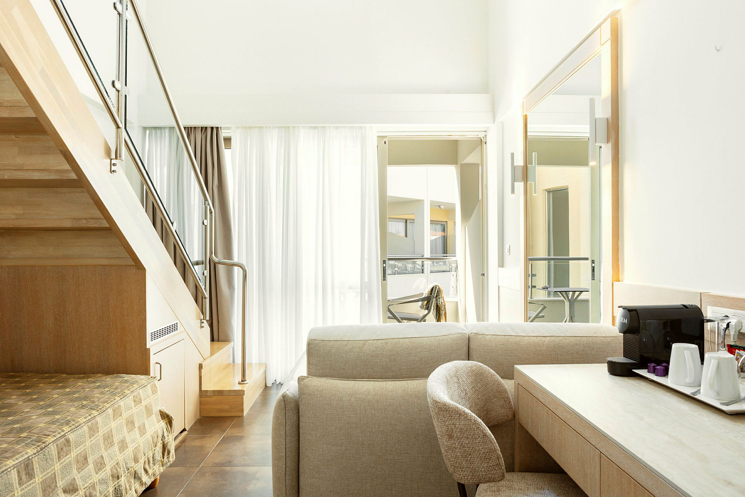 Interiørbillede af et moderne hotelværelse med en trappe, siddegruppe og et skrivebord med kaffemaskine. (AI-genereret tekst)