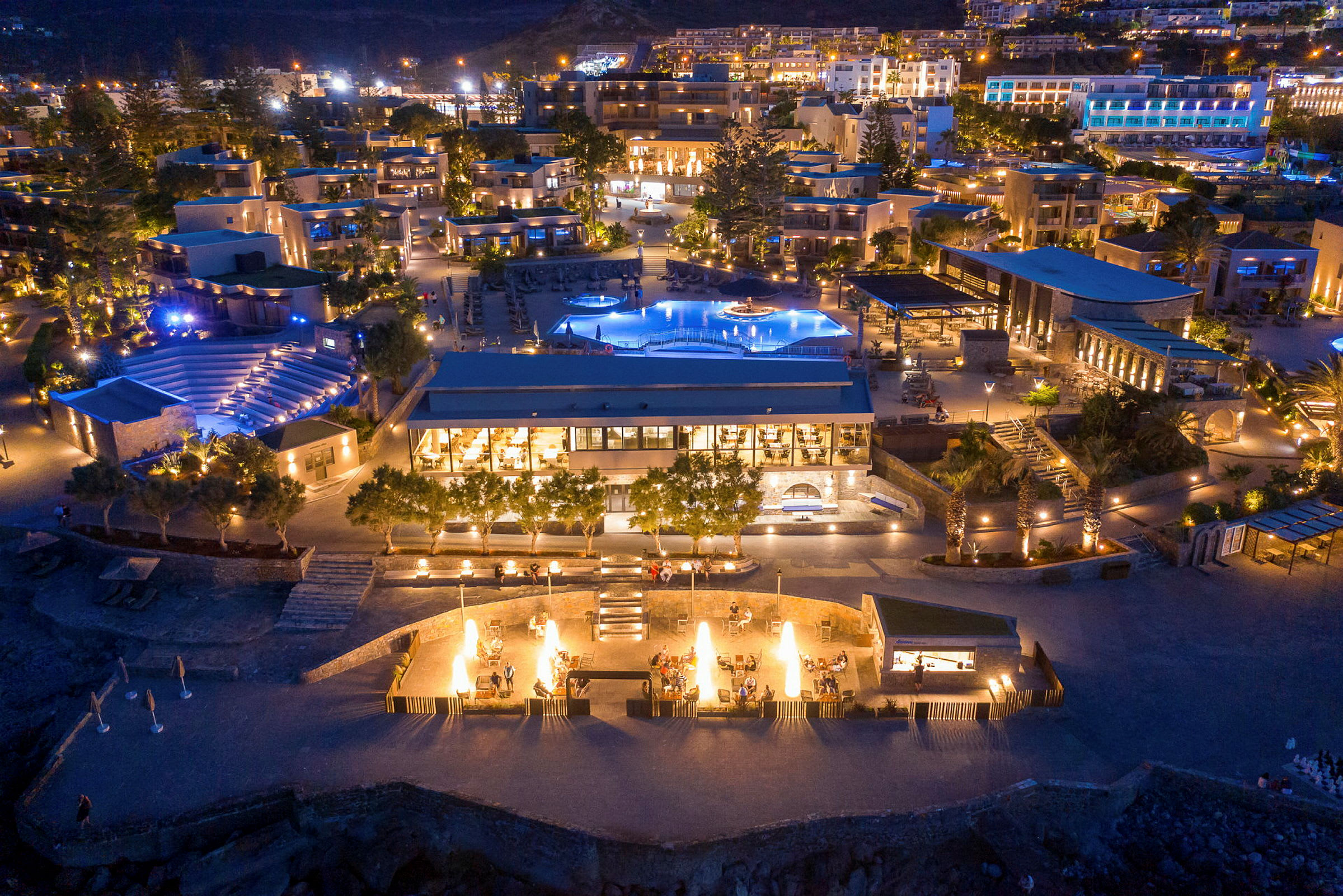 En resort med flere bygninger, pools og udendørsområder oplyst om aftenen. (AI-genereret tekst)