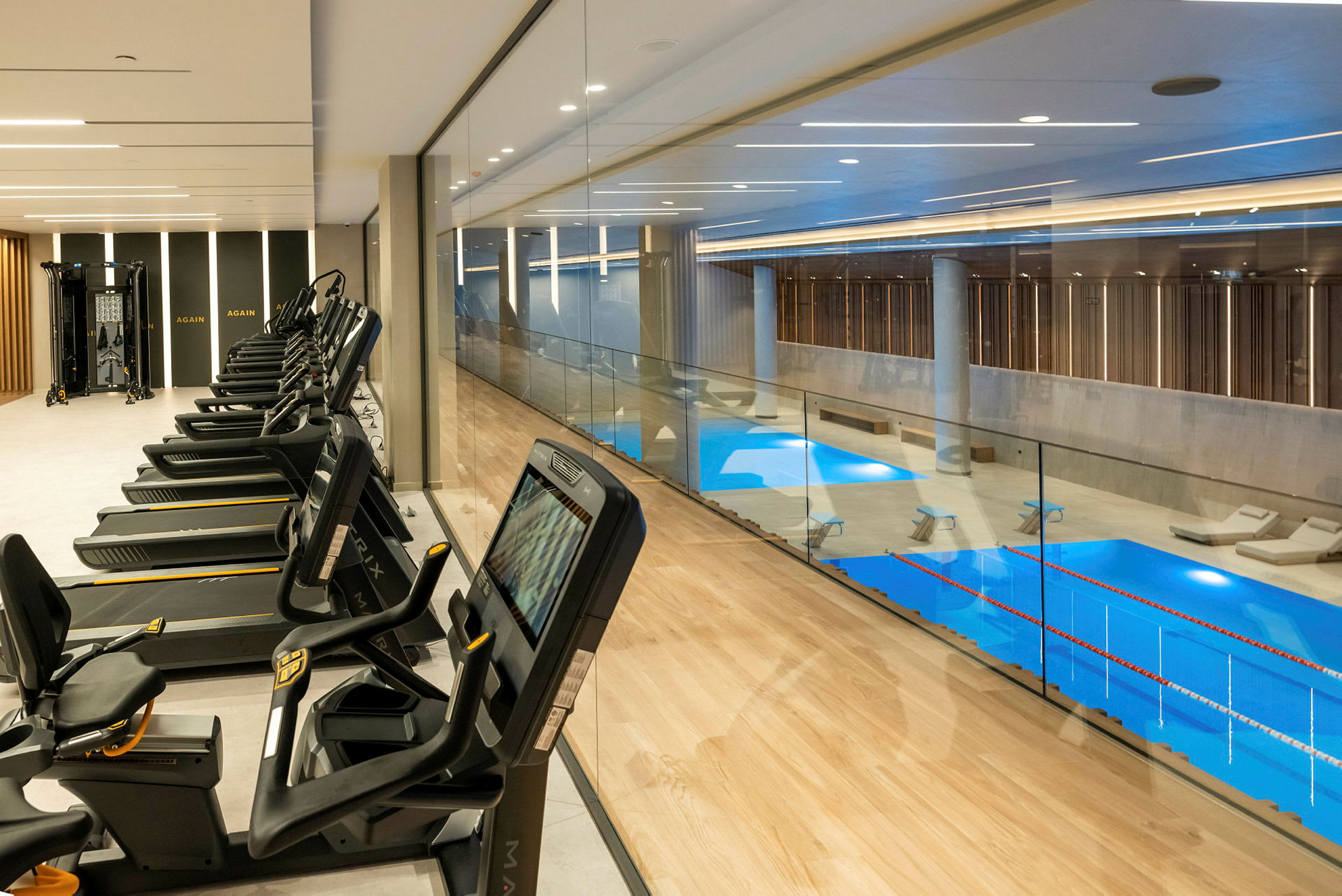 Billede af et moderne fitnesscenter med træningsmaskiner ved siden af en turkis indendørs pool. (AI-genereret tekst)