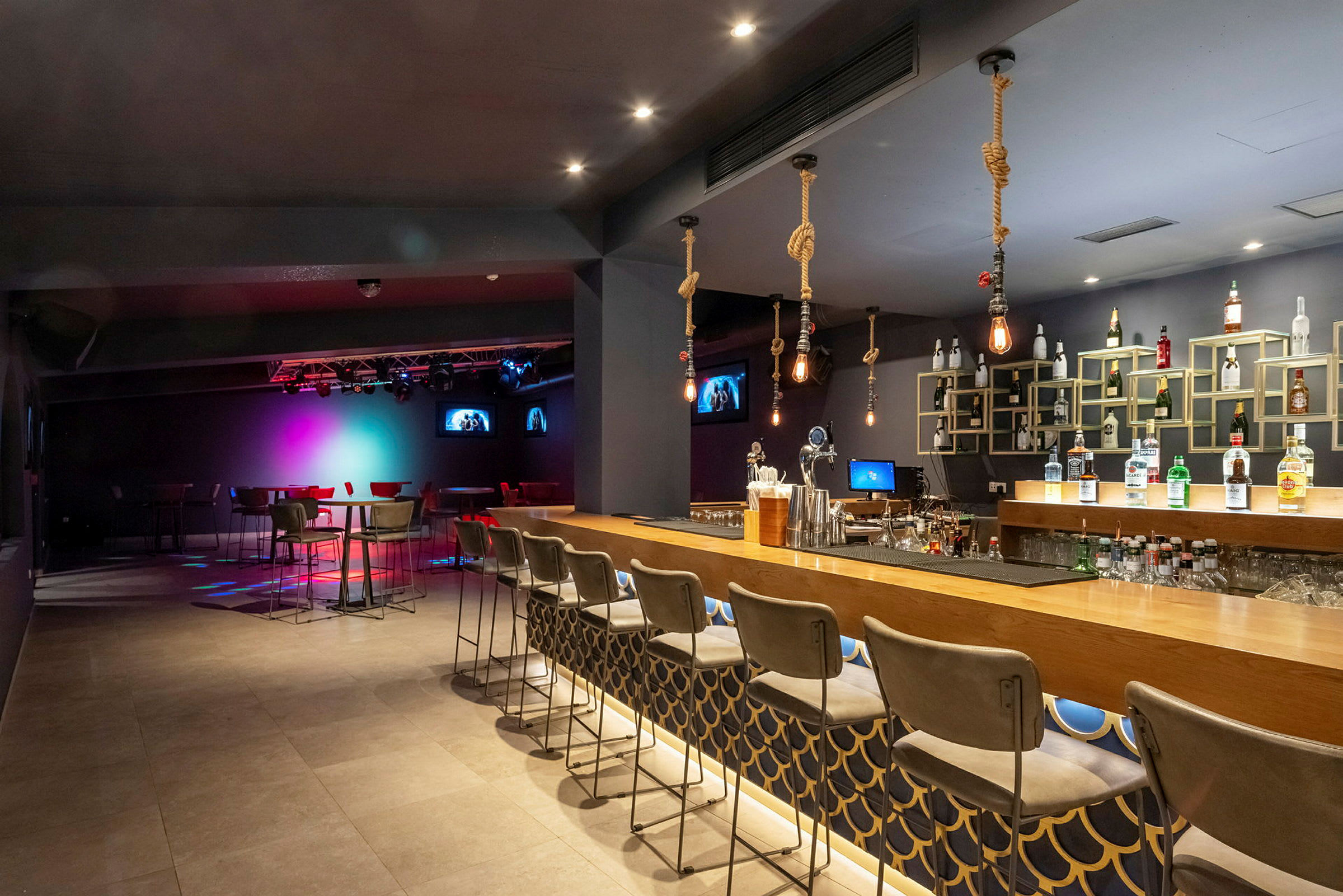 Indendørs billede af en bar med siddepladser og en oplyst scene i baggrunden. (AI-genereret tekst)