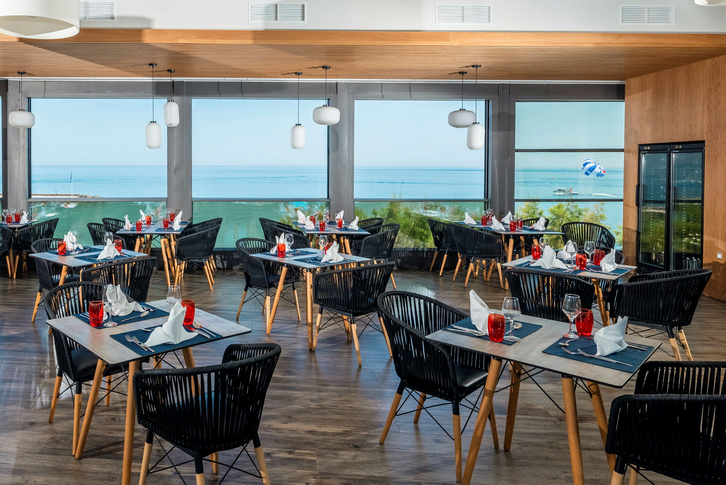 En restaurant med dækkede borde og udsigt over havet gennem store vinduer. (AI-genereret tekst)