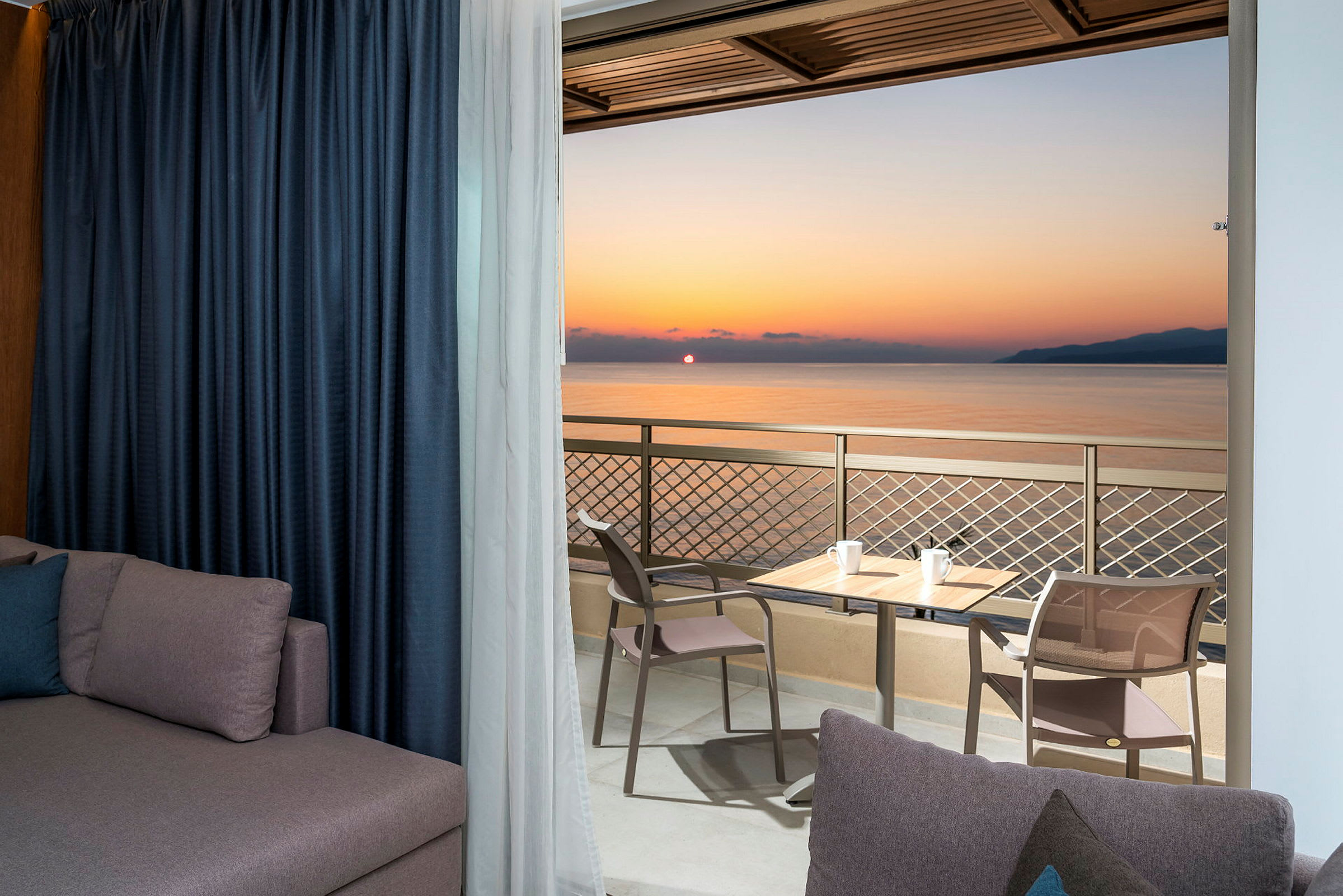 Udsigt fra en balkon med en solnedgang over havet, bord og stole placeret på balkonen. (AI-genereret tekst)