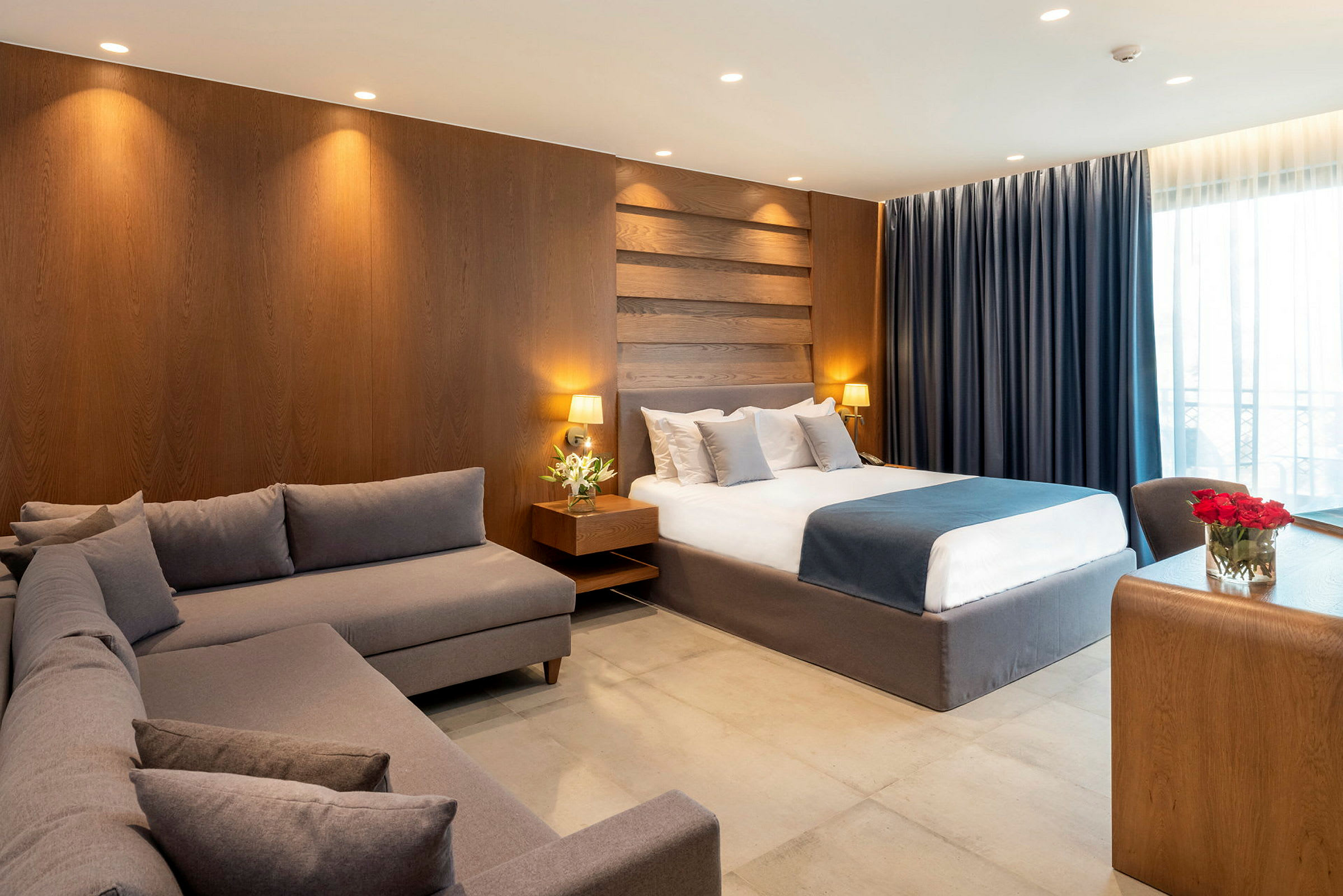 Et hotelværelse med en stor seng, en grå sofa og et skrivebord af træ. (AI-genereret tekst)