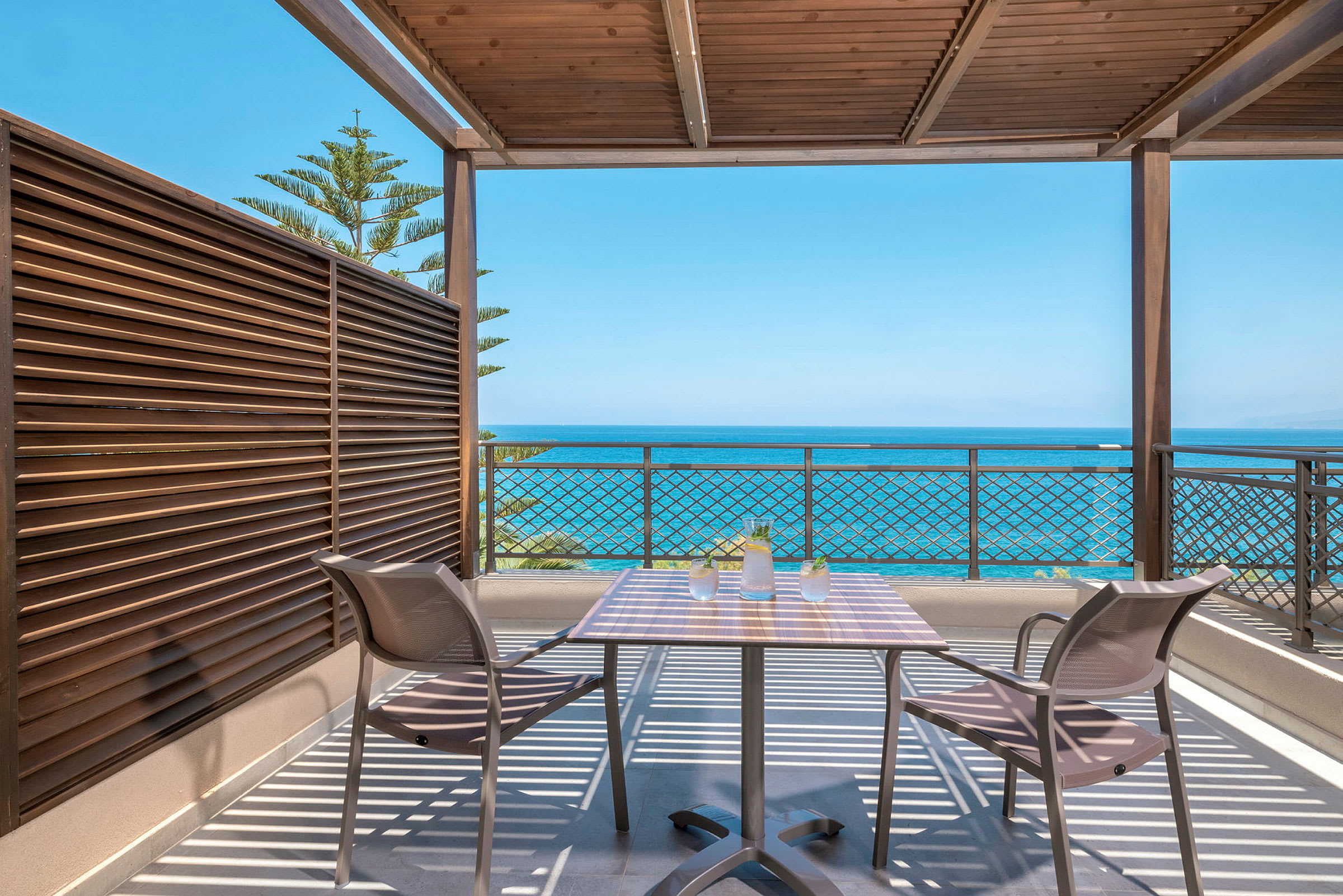 Terrasse med bord og stole under tag med udsigt til havet. (AI-genereret tekst)