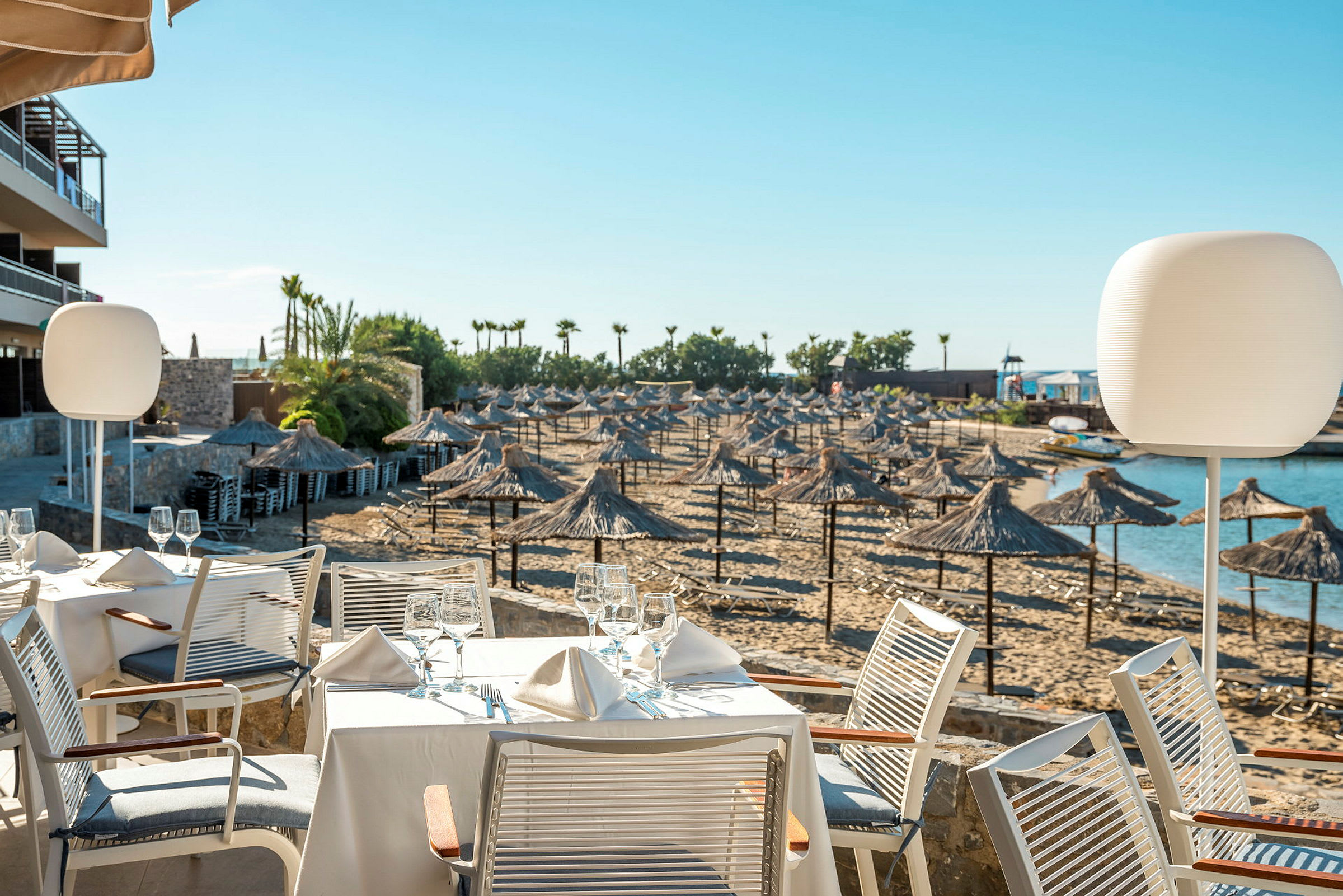 Udendørs restaurant med borde tæt på en sandstrand med parasoller og liggestole. (AI-genereret tekst)